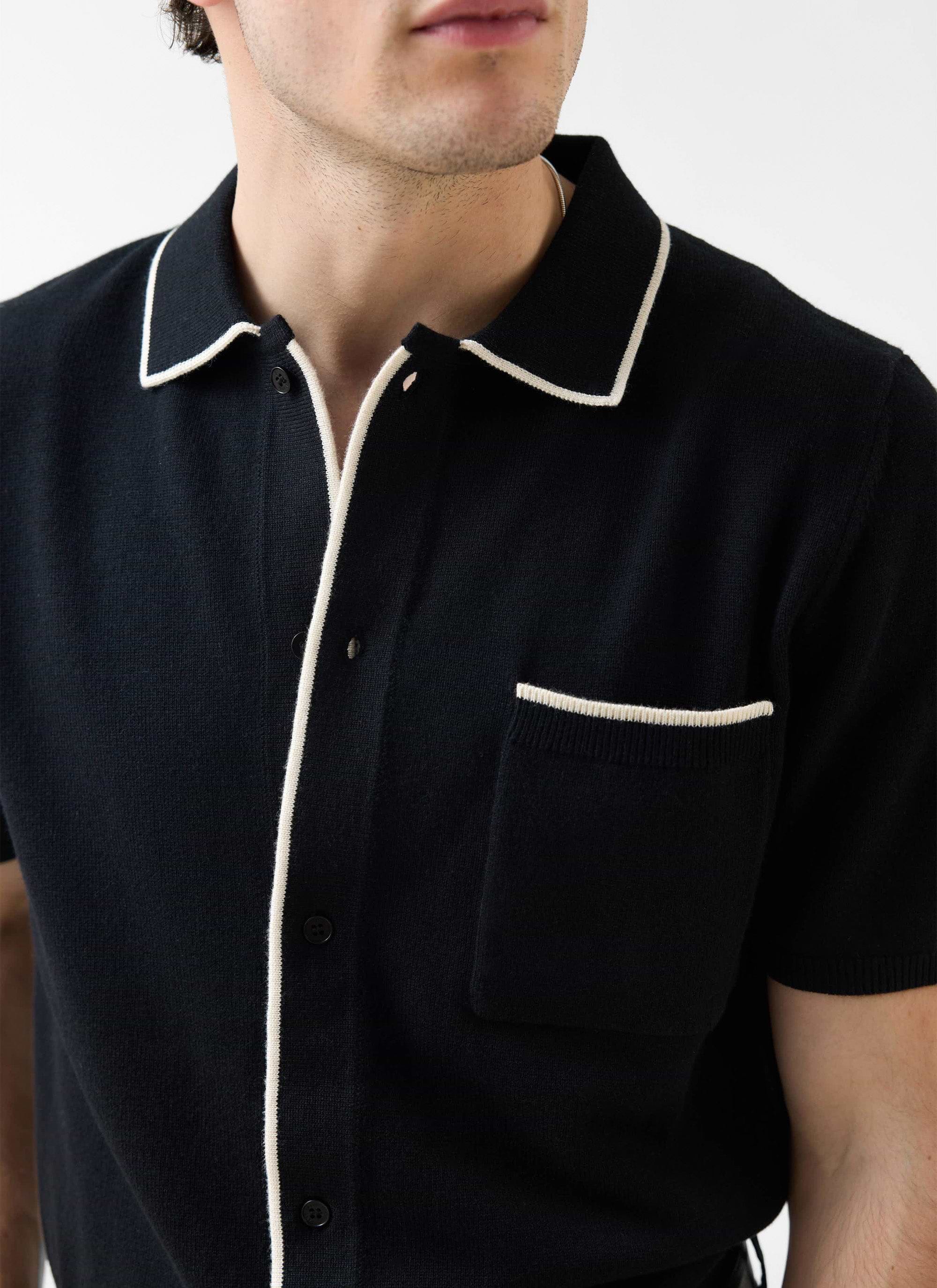 A close-up of a model wearing the Percival Contrast Trim Knitted Shirt in black with ecru detailing on the collar and pocket.