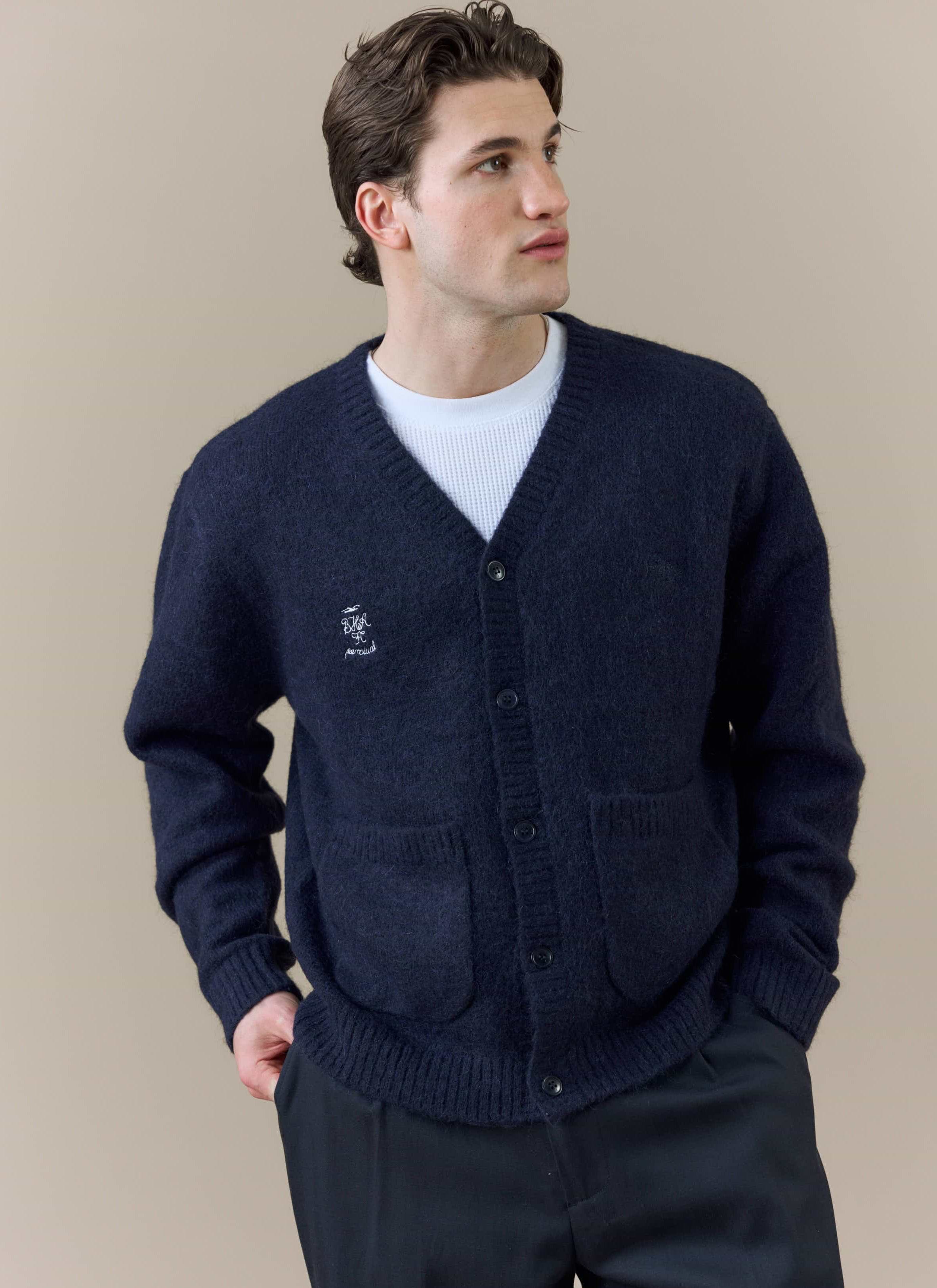 A model wears the Percival x Brighton & Hove Albion F.C. White Glove Cardigan in navy, showing the collaborative embroidery.