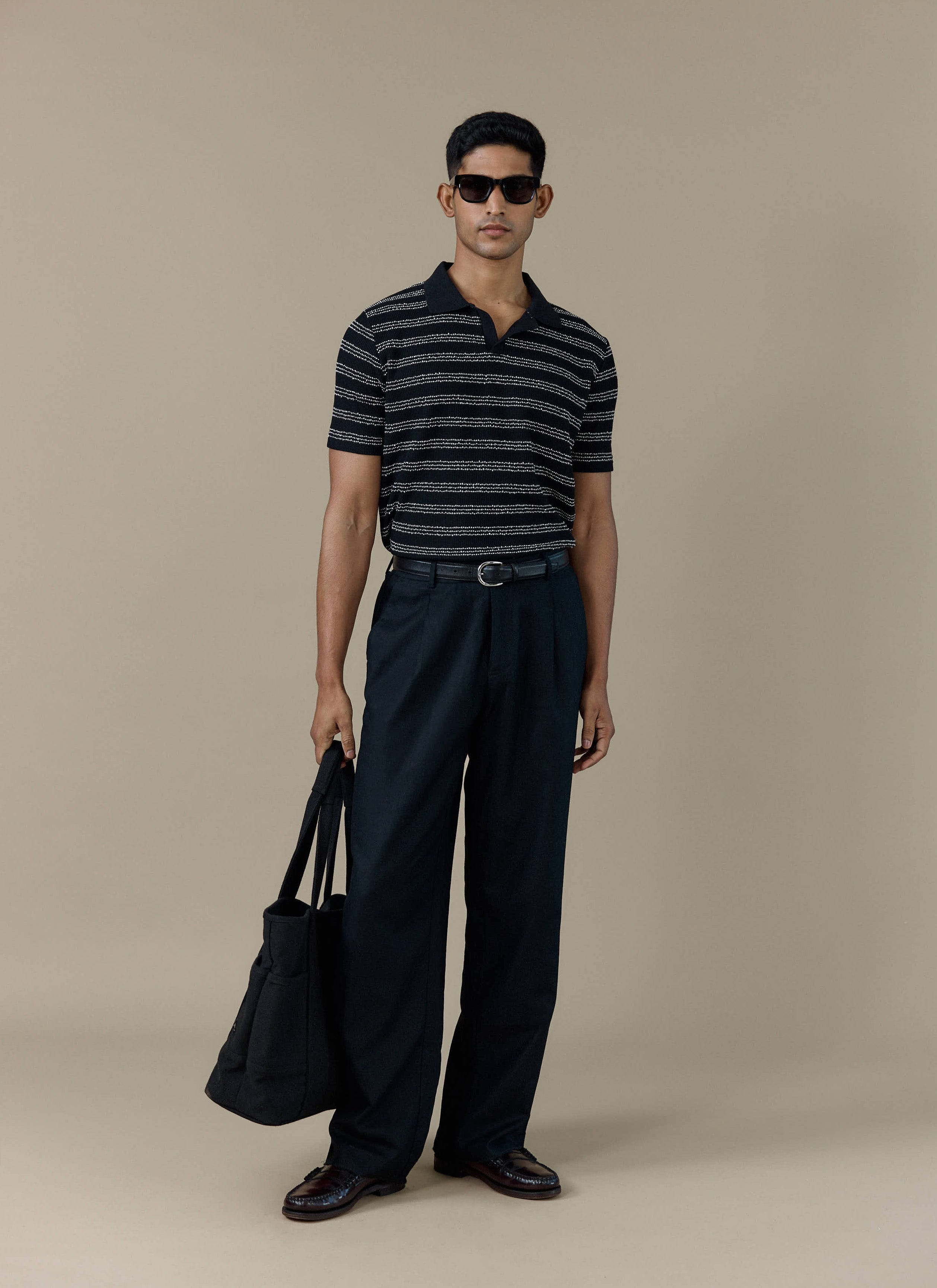 Model wearing the Percival Laurent Boxy Polo in black stripe, paired with black trousers and sunglasses.