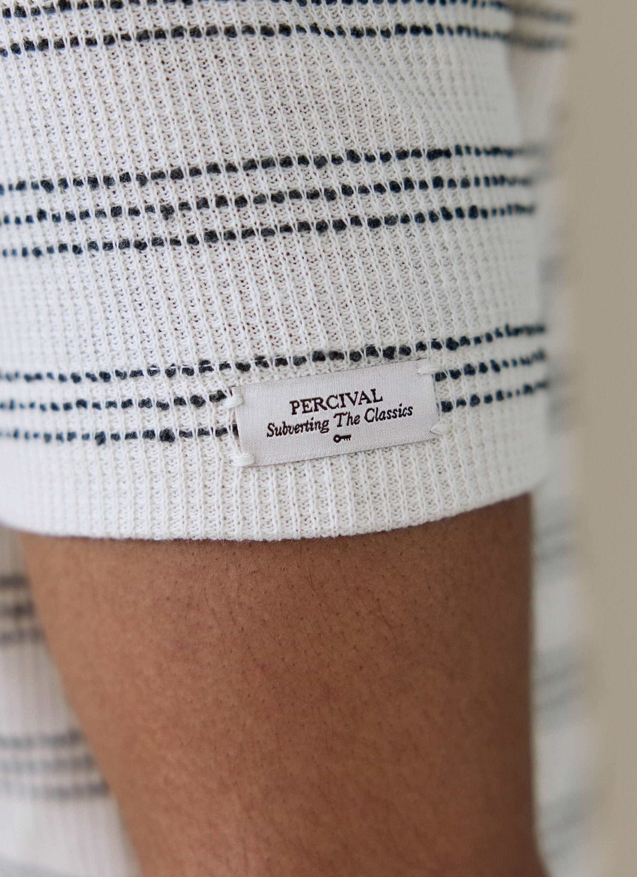 Close-up of the Percival sleeve label on the cream Laurent Boxy Polo, showing the ribbed fabric and stripe detail.