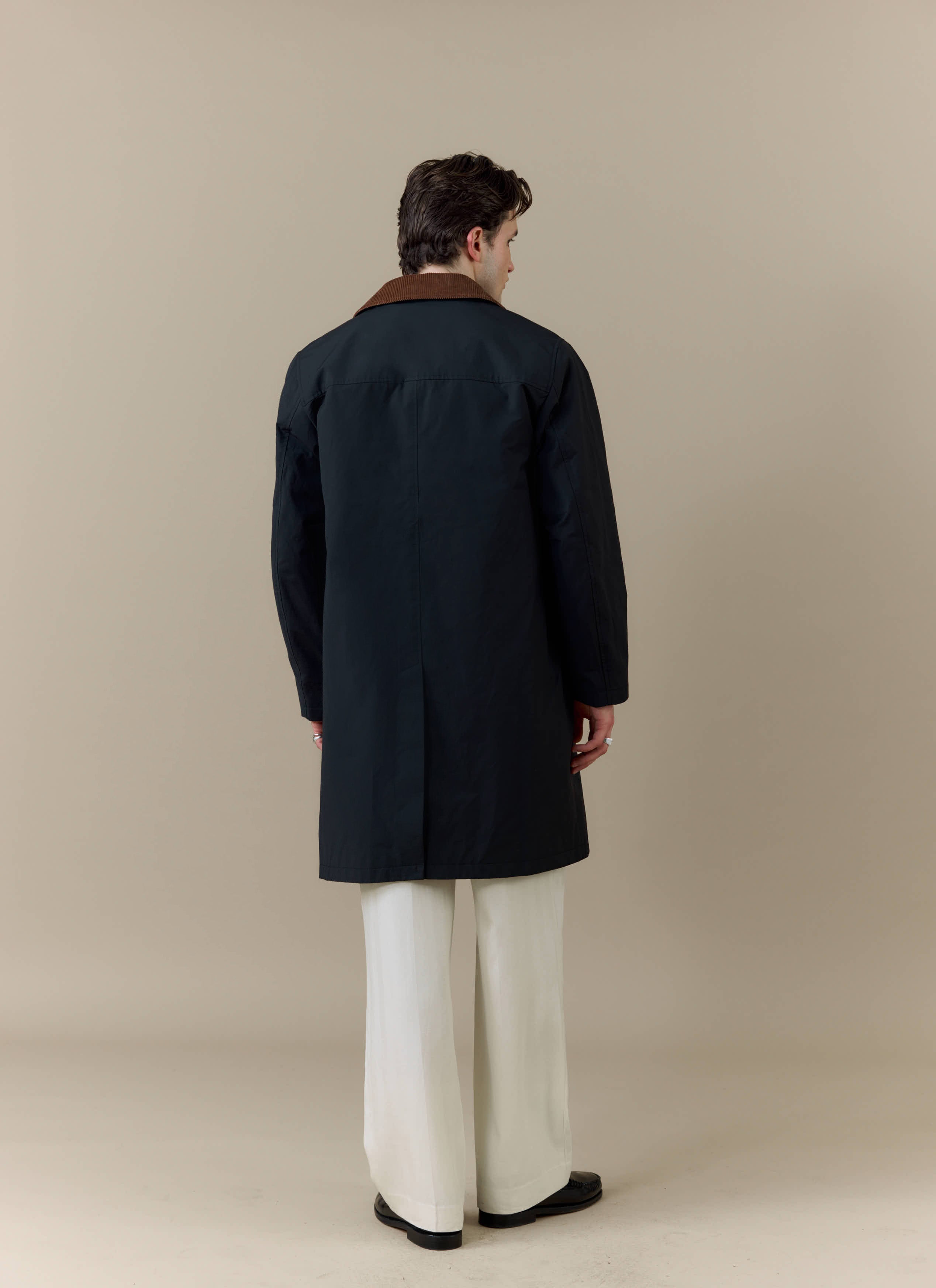 Back view of a model wearing the Percival Cord Collar Relaxed Trench Coat in black with a brown corduroy collar.