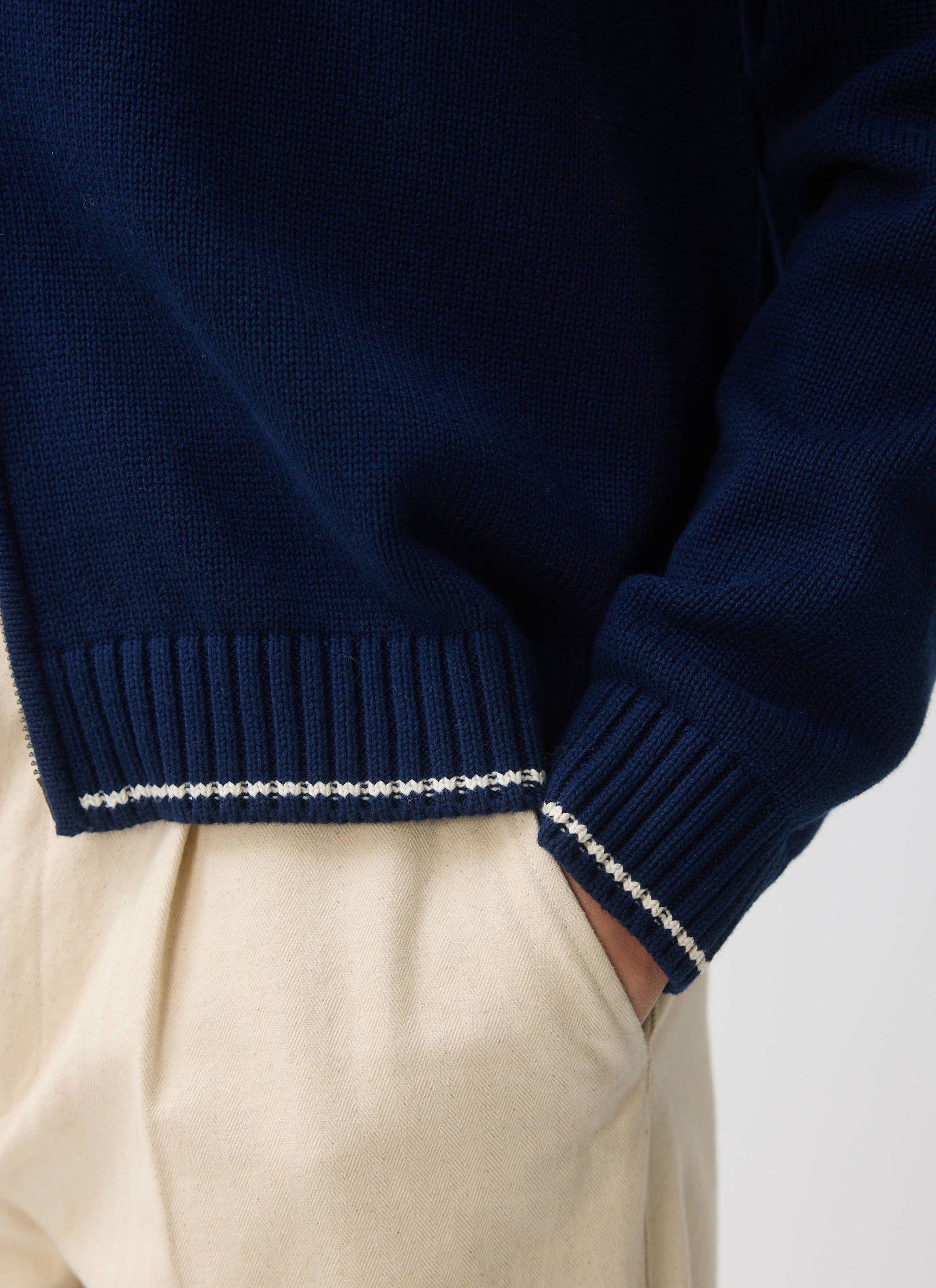 A close-up of the ribbed hem on the Percival Gardner Dense Knitted Zip Cardigan in navy, showing the white stitch detail.