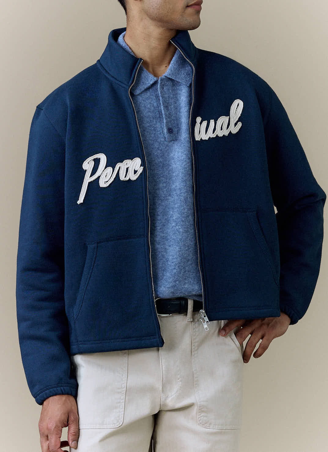 A model wears the navy Curtis Boxy Zip Funnel Neck Harrington from Percival, styled over a blue polo and light trousers.