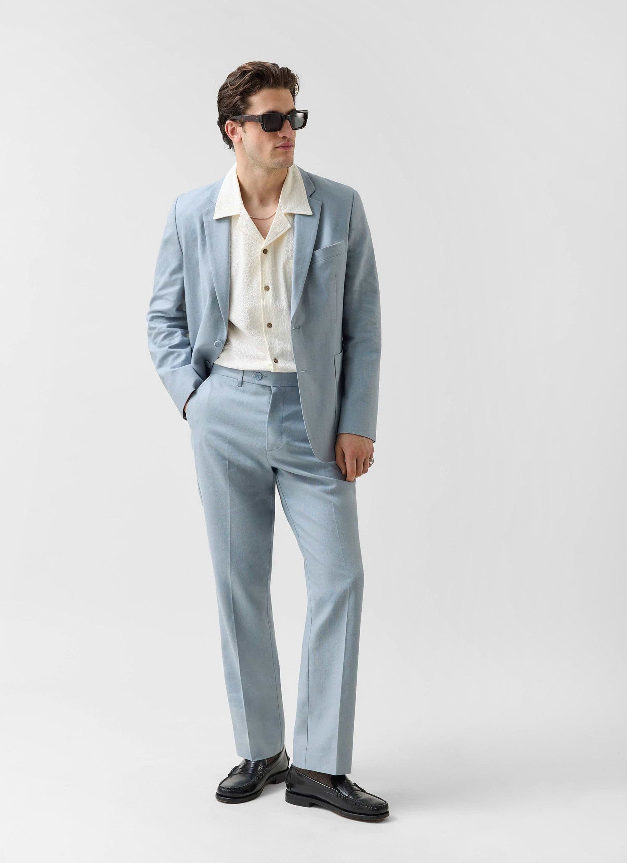 Model wears the Percival light blue linen suit with a cream shirt, black loafers and sunglasses.