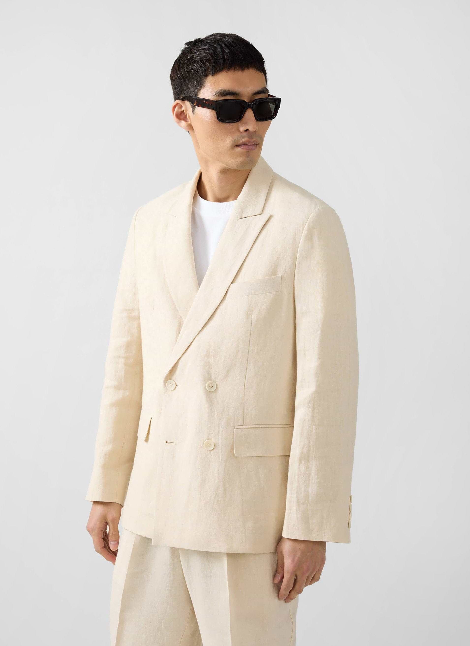 A model wears the Percival Clifton Double Breasted Blazer in cream linen with a white t-shirt and black sunglasses.