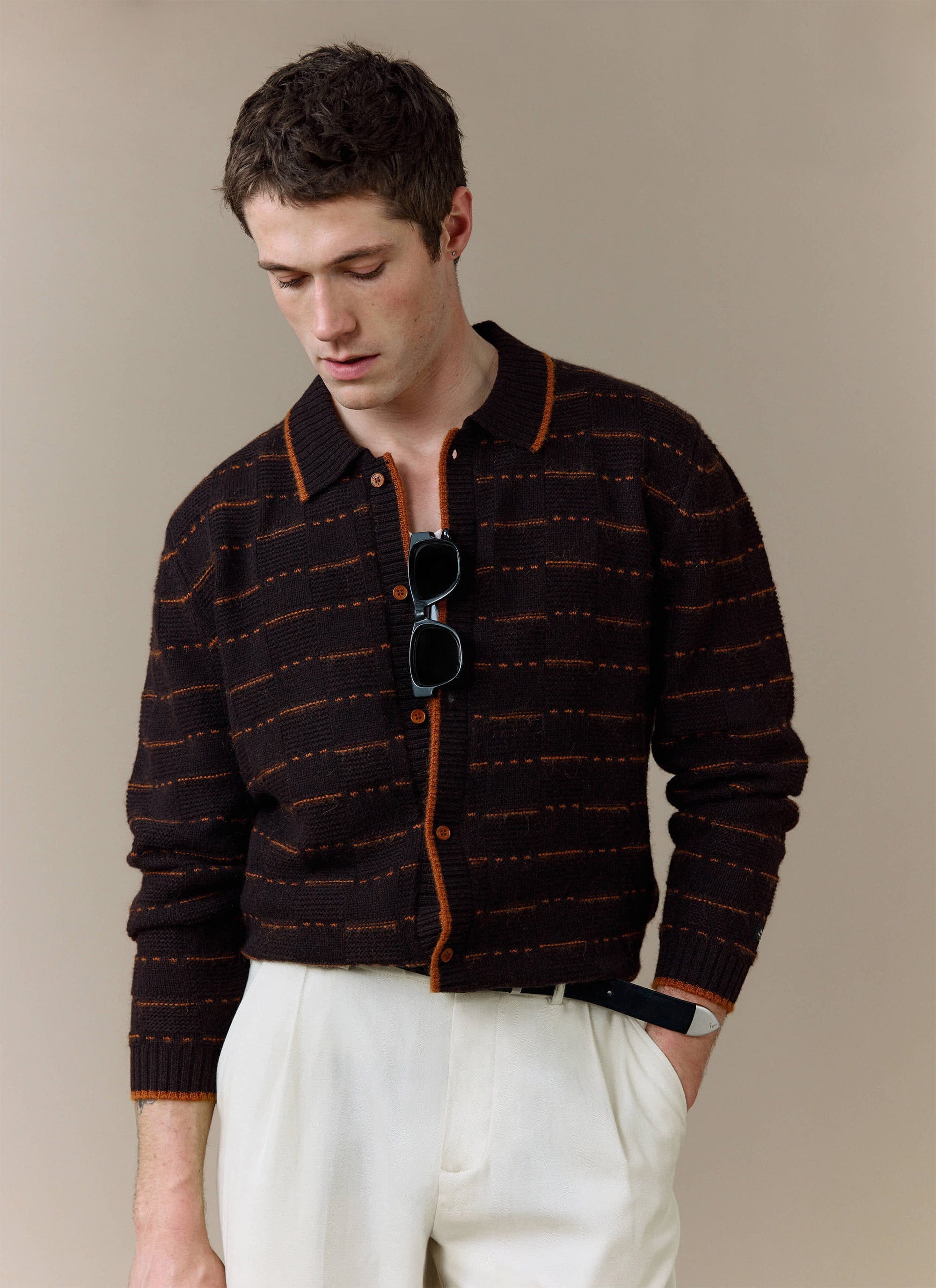 A model wears the brown Addison Long Sleeve Knitted Shirt from Percival, styled with smart white trousers.