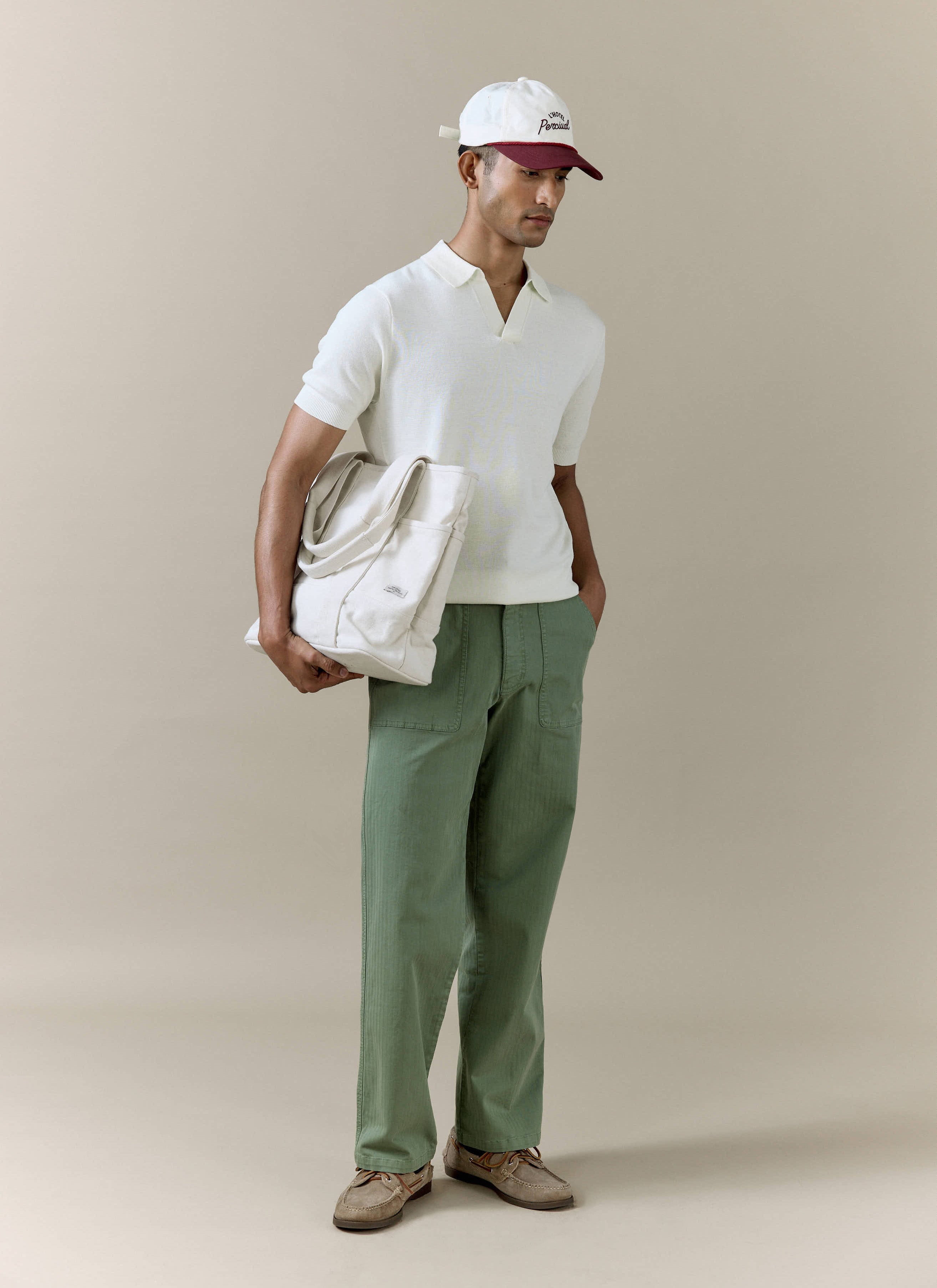 Cream linen-blend Laurence Knitted Polo by Percival, styled with an open Johnny collar, green trousers and a tote bag.