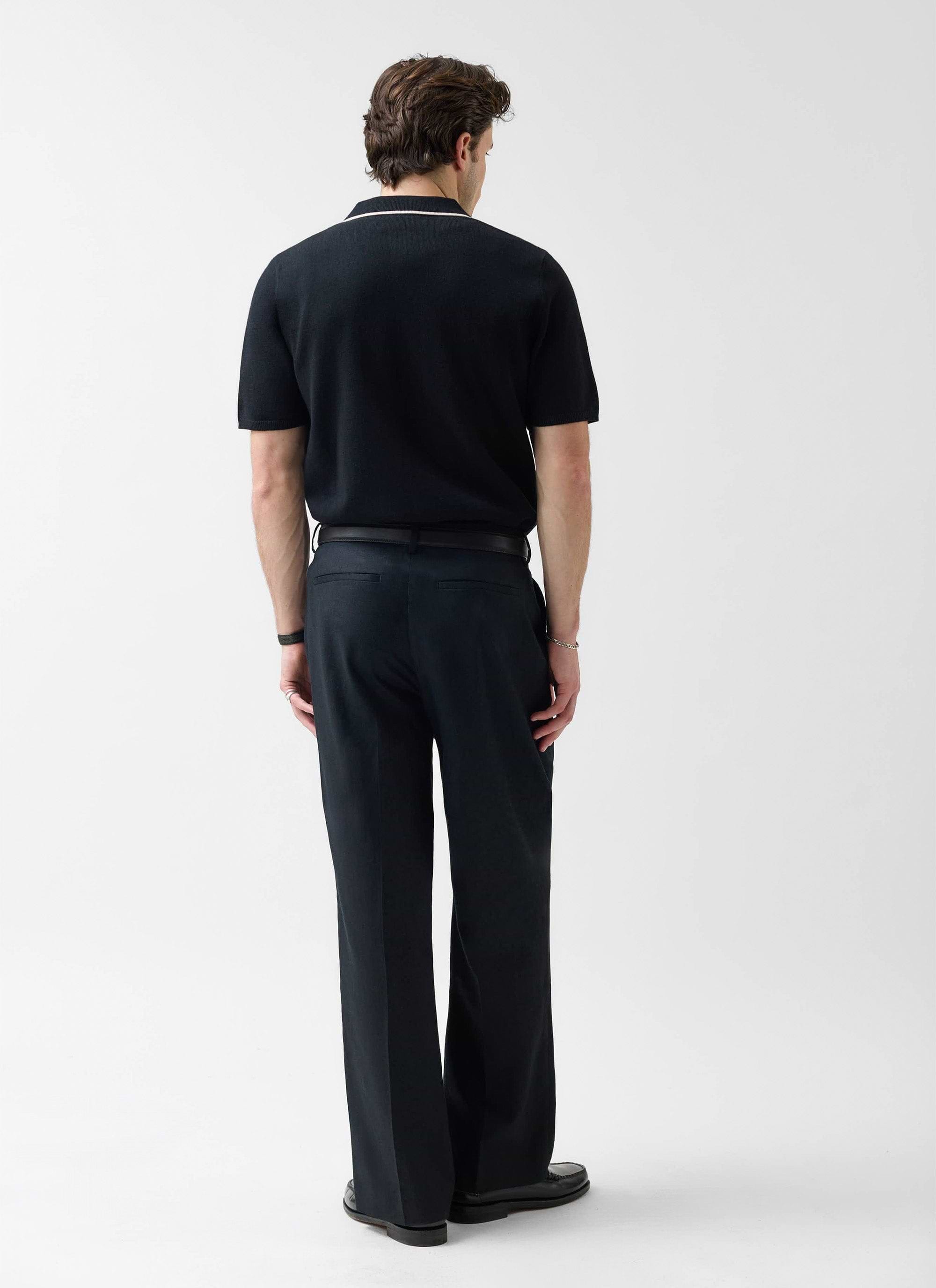 A model seen from behind in the Percival Contrast Trim Knitted Shirt in black with ecru trim, styled with black trousers.