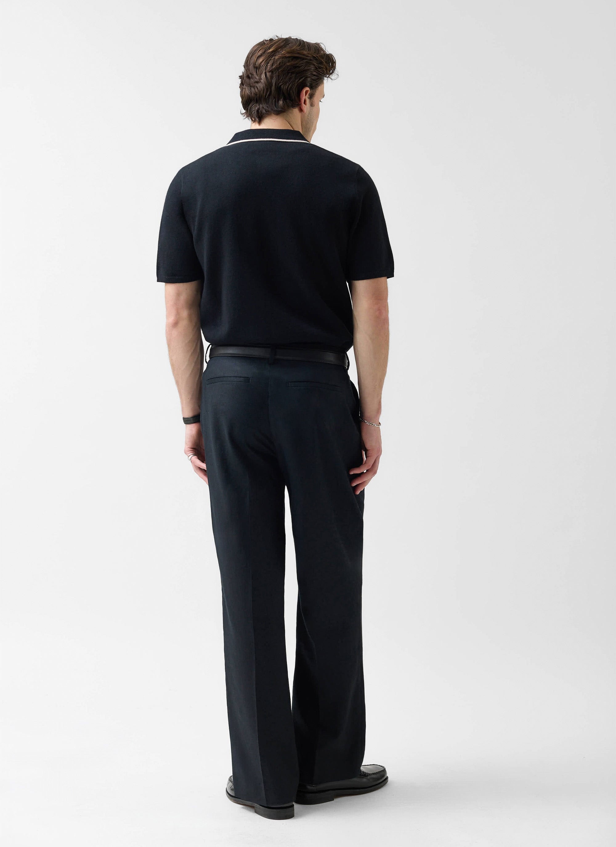 A model seen from behind in the Percival Contrast Trim Knitted Shirt in black with ecru trim, styled with black trousers.