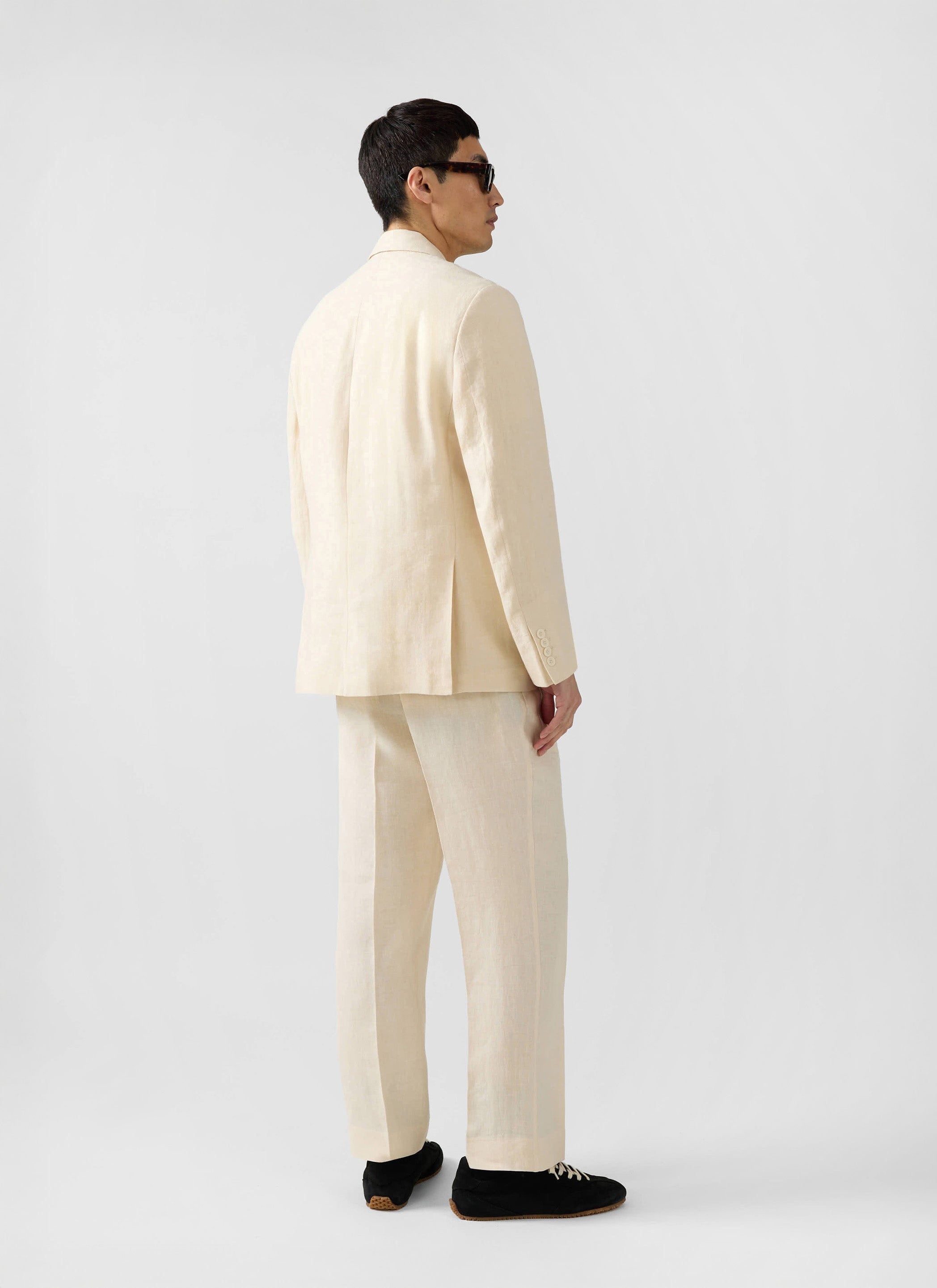 A model wears the Percival Clifton Double Breasted Blazer in cream linen, showing the back and side view.