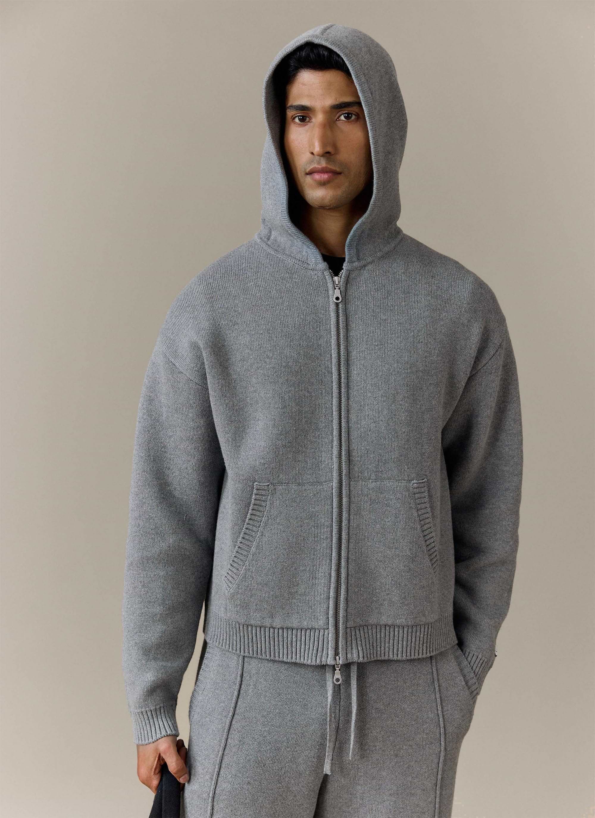 A model wears the grey Chronicle Knitted Hoodie from Percival with the hood up, looking directly at the camera.