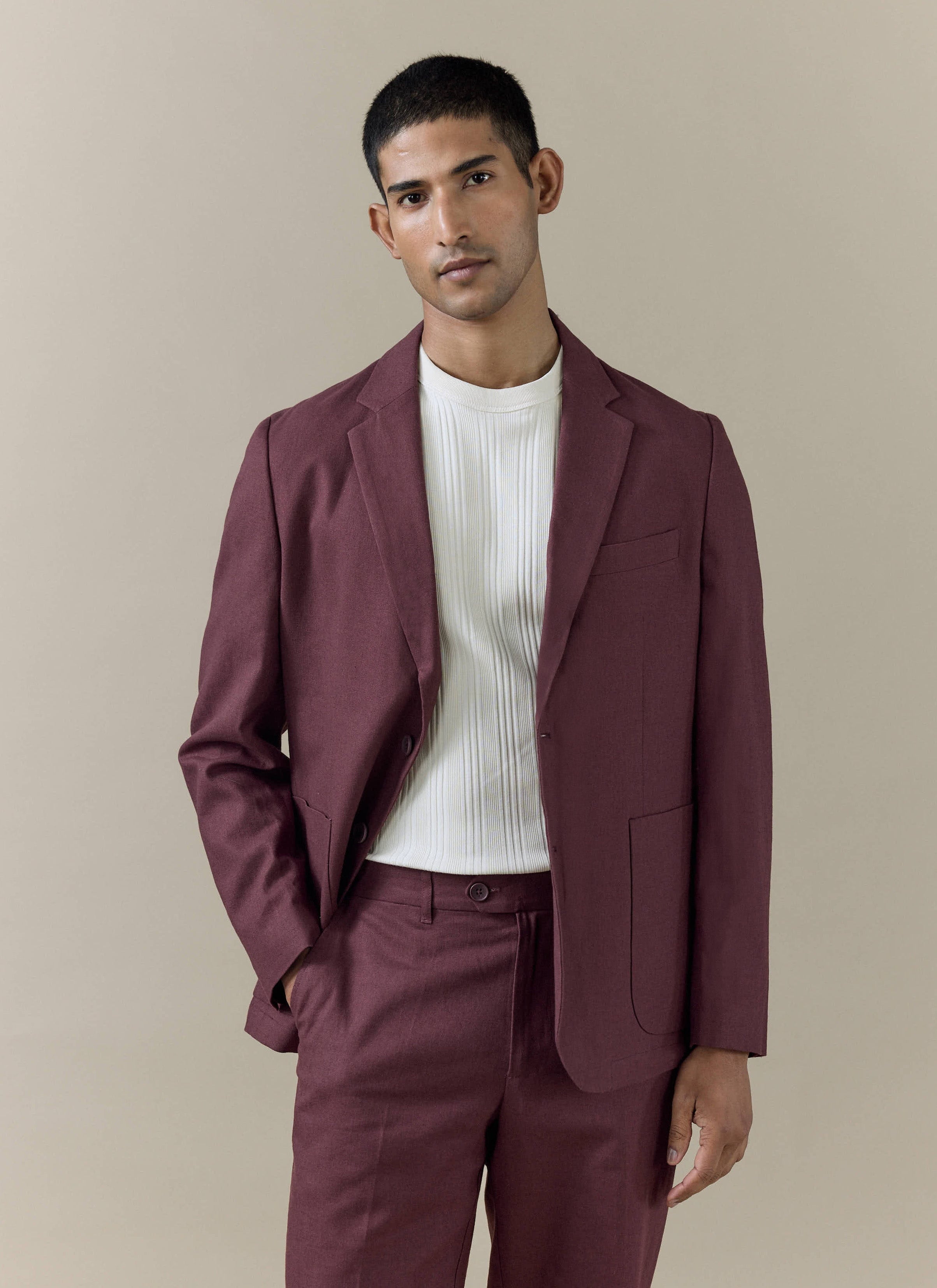A model wears the Percival Tailored Linen Blazer in Merlot, styled with matching trousers and a white ribbed top.