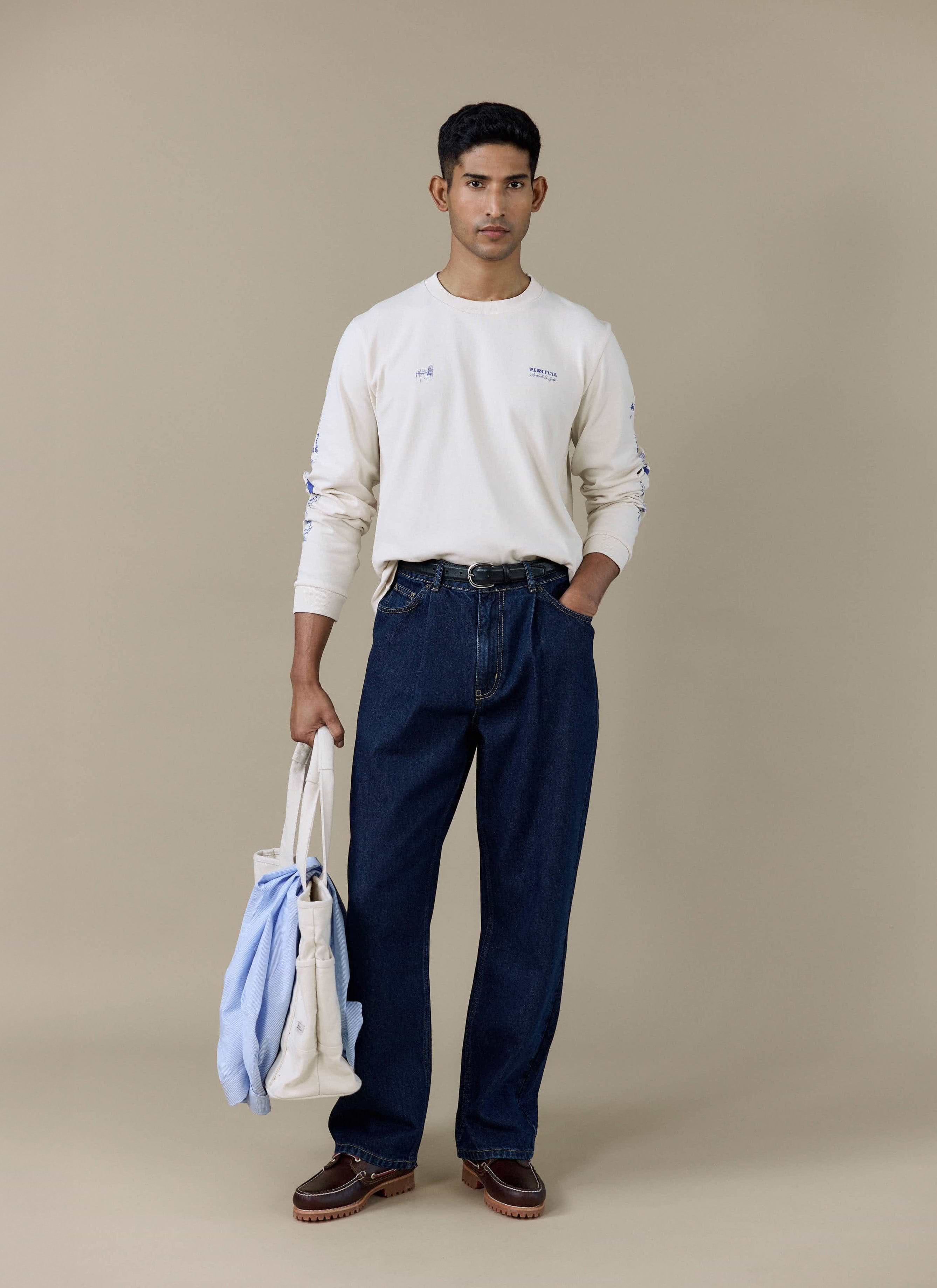 Model wears the Percival Harlow Fine Wines Long Sleeve T Shirt in cream organic cotton, styled with dark indigo jeans.