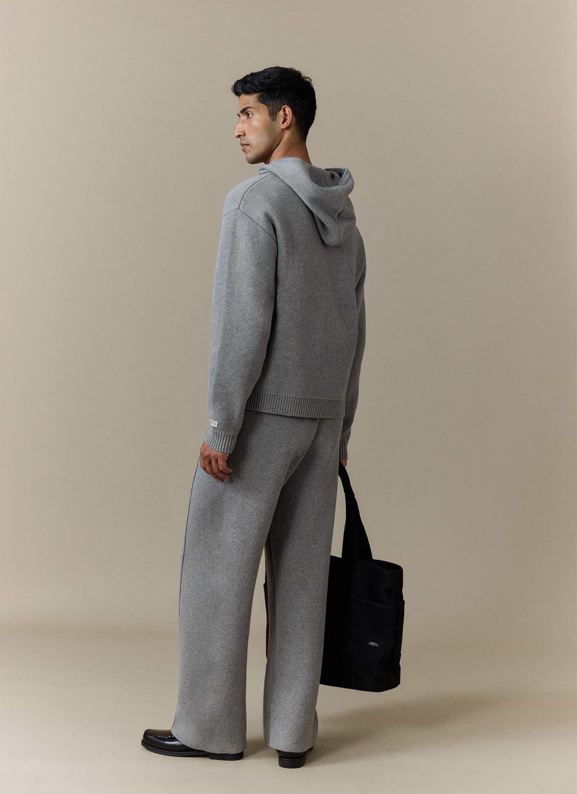 A model looking over his shoulder wearing the Percival Chronicle Knitted Hoodie in grey with matching knitted trousers.