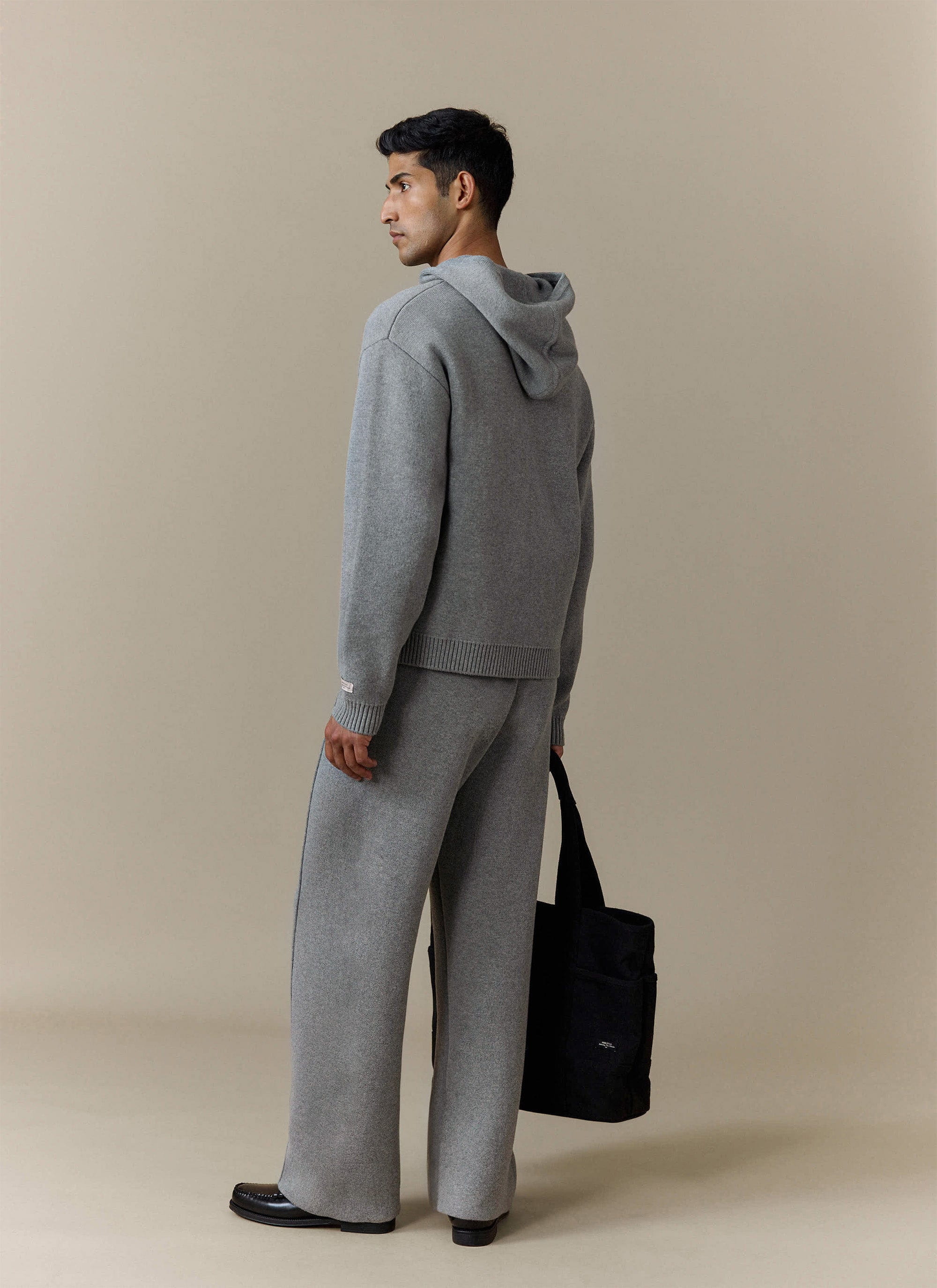 A model looking over his shoulder wearing the Percival Chronicle Knitted Hoodie in grey with matching knitted trousers.