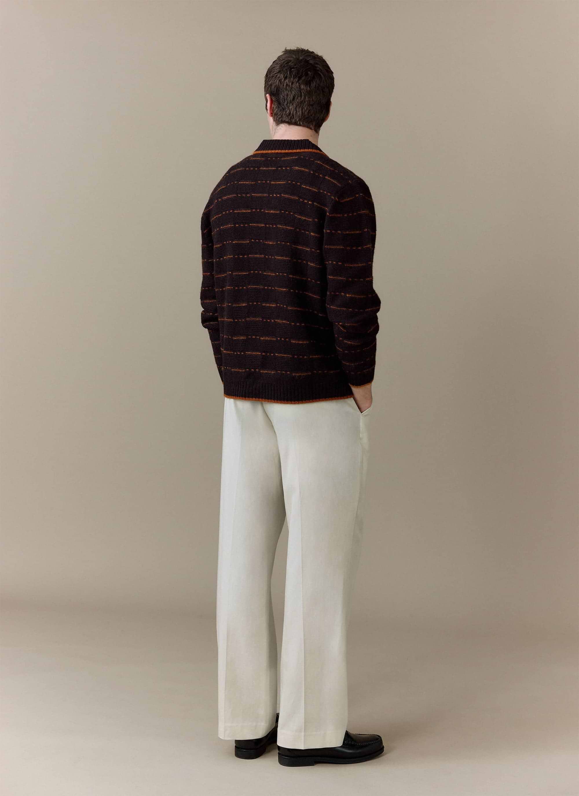 Back view of a model wearing the Percival Addison Long Sleeve Knitted Shirt in brown, styled with cream trousers.