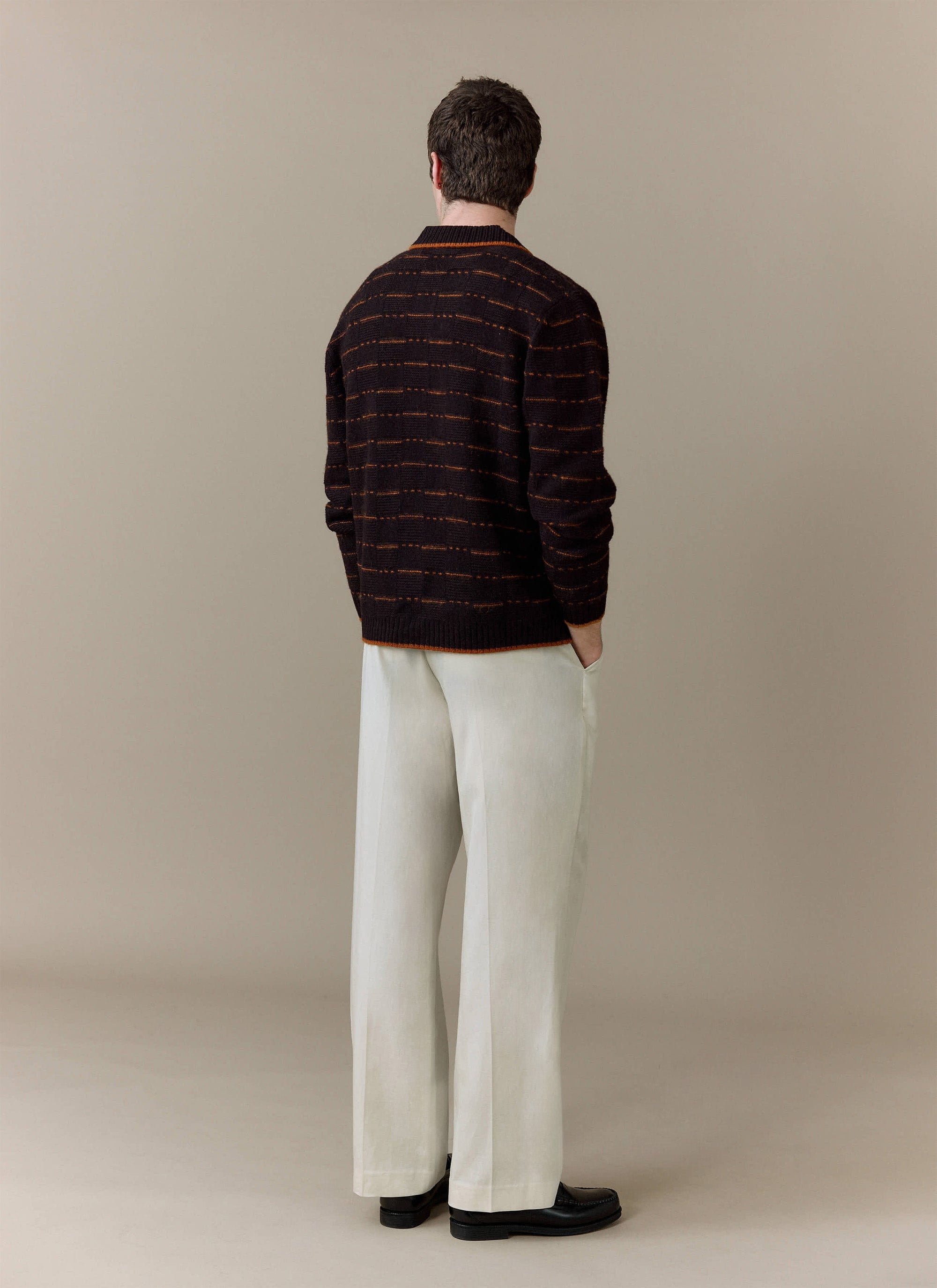Back view of a model wearing the Percival Addison Long Sleeve Knitted Shirt in brown, styled with cream trousers.
