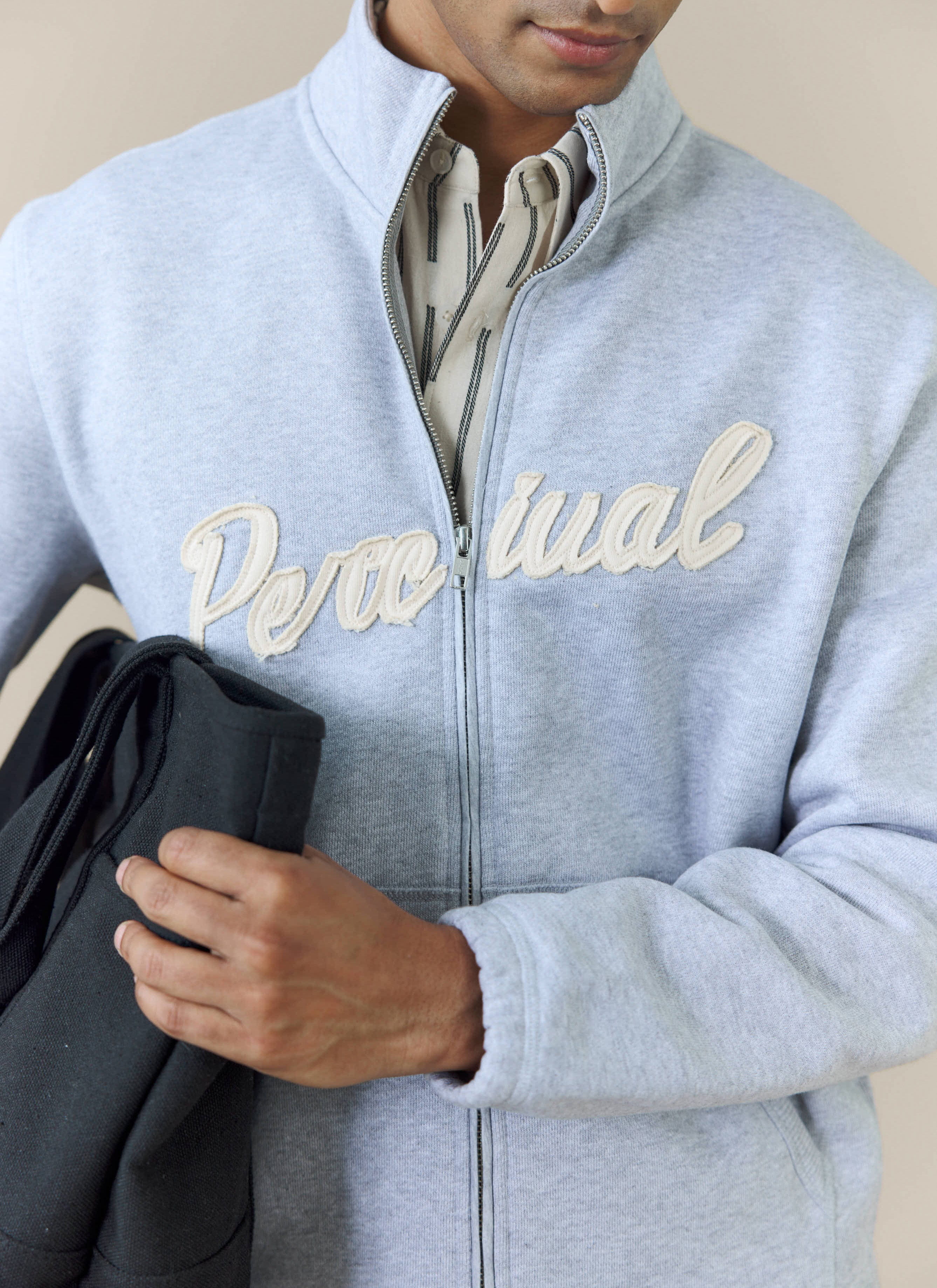 A close-up of a model wearing the Percival Curtis Boxy Zip Funnel Neck Sweatshirt showing the cream appliqué logo.