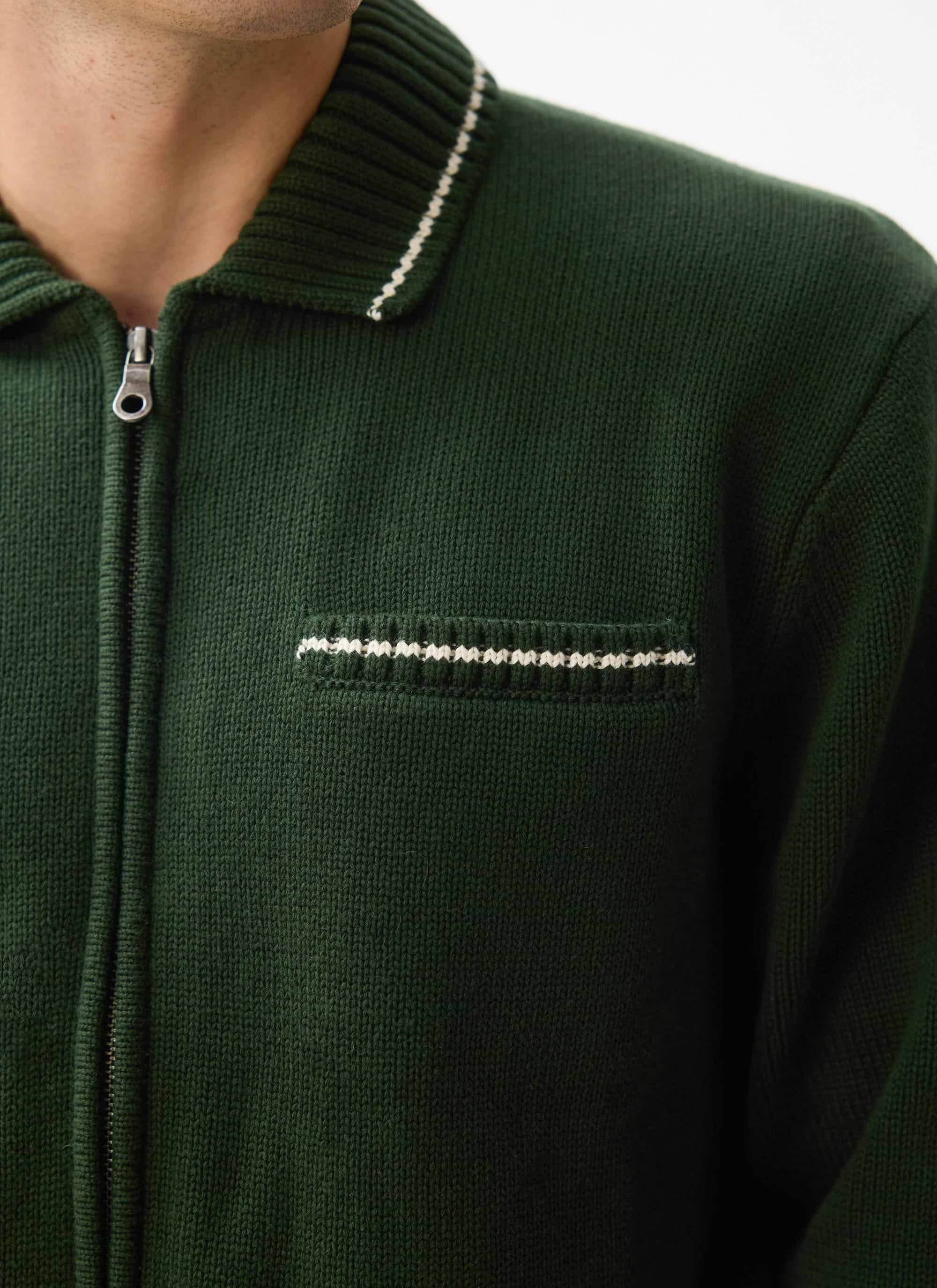 Close up of a model wearing the Percival Gardner Dense Knitted Zip Cardigan in forest green, showing contrast stitching.
