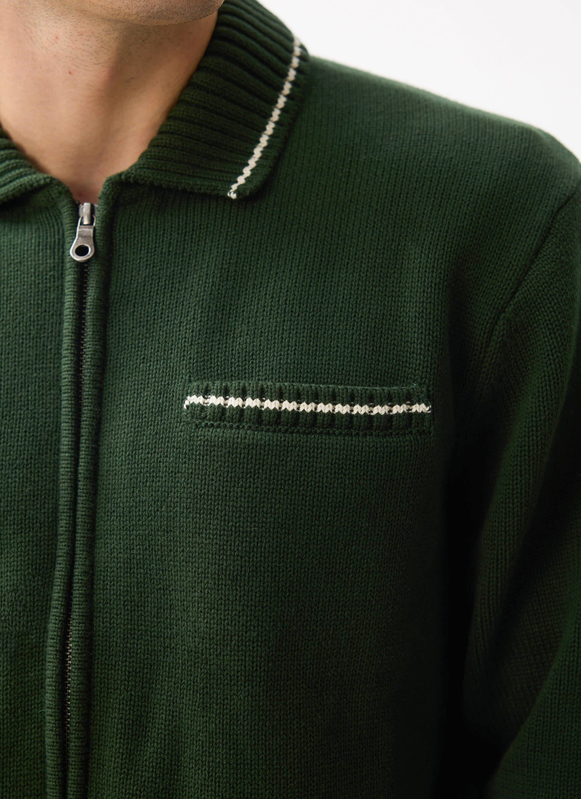 Close up of a model wearing the Percival Gardner Dense Knitted Zip Cardigan in forest green, showing contrast stitching.