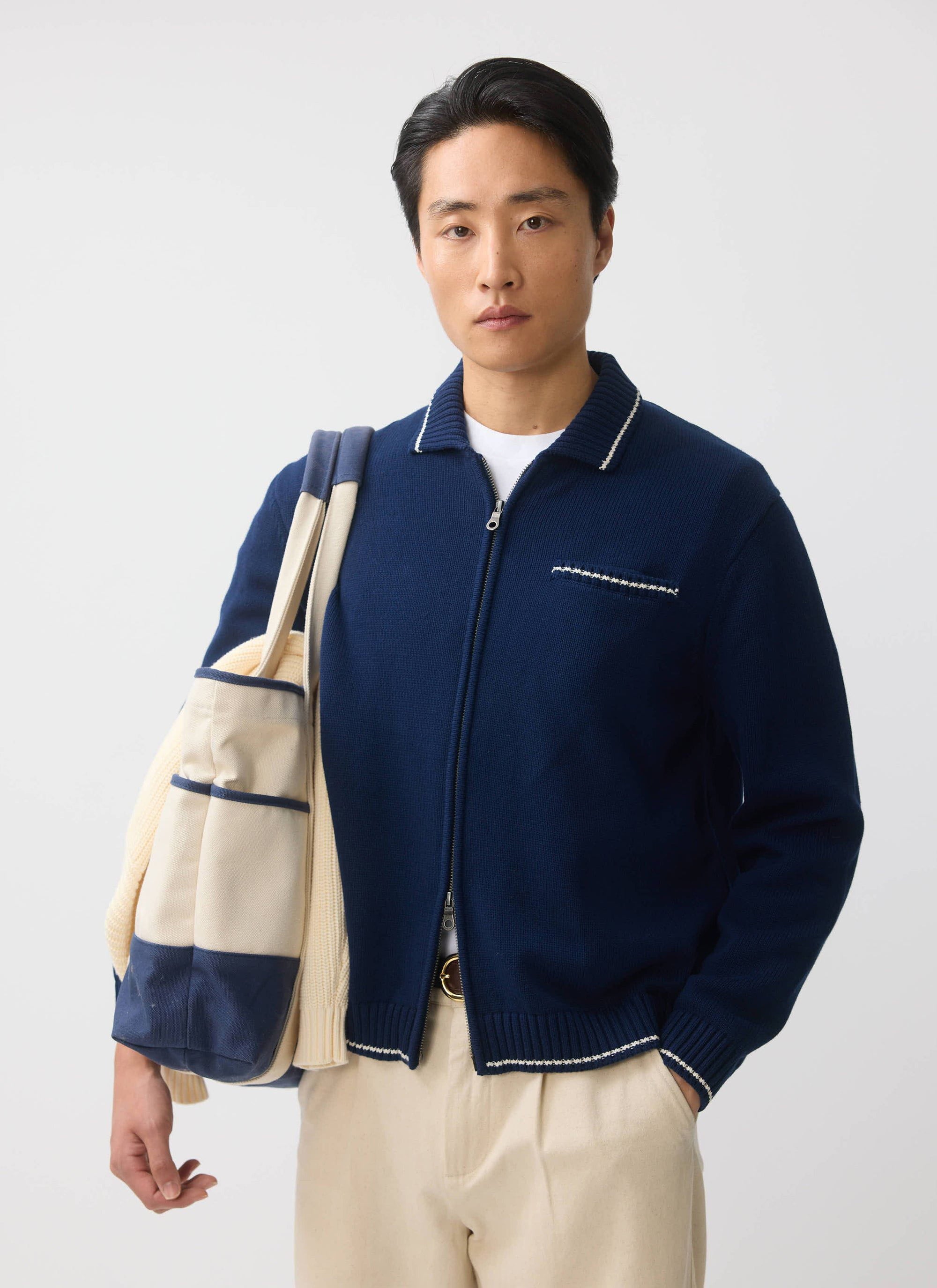 A model wears the Percival Gardner zip cardigan in navy, styled with cream trousers and carrying a canvas tote bag.