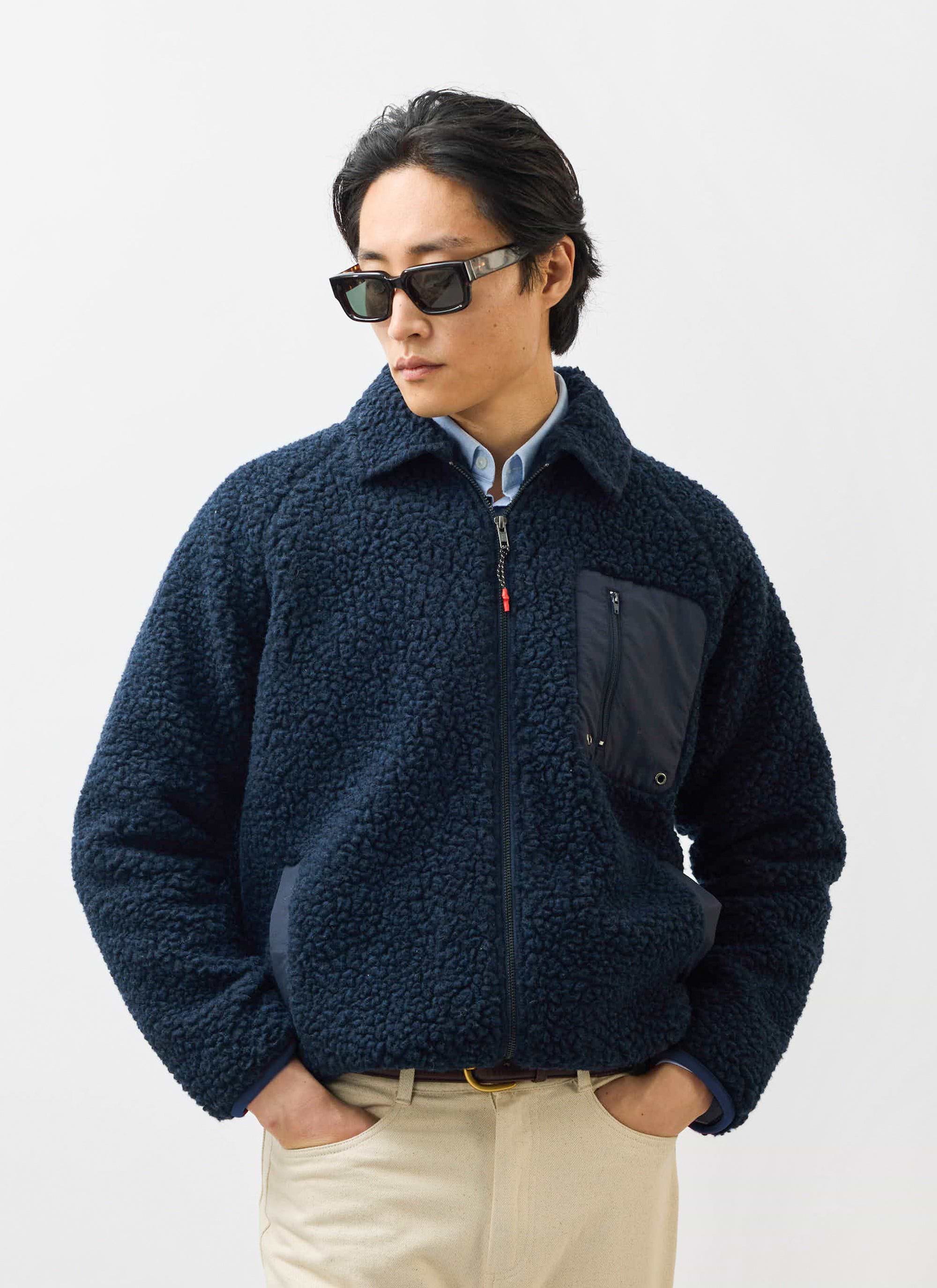 A model wears the Percival navy wool fleece jacket with sunglasses and cream trousers against a white background.