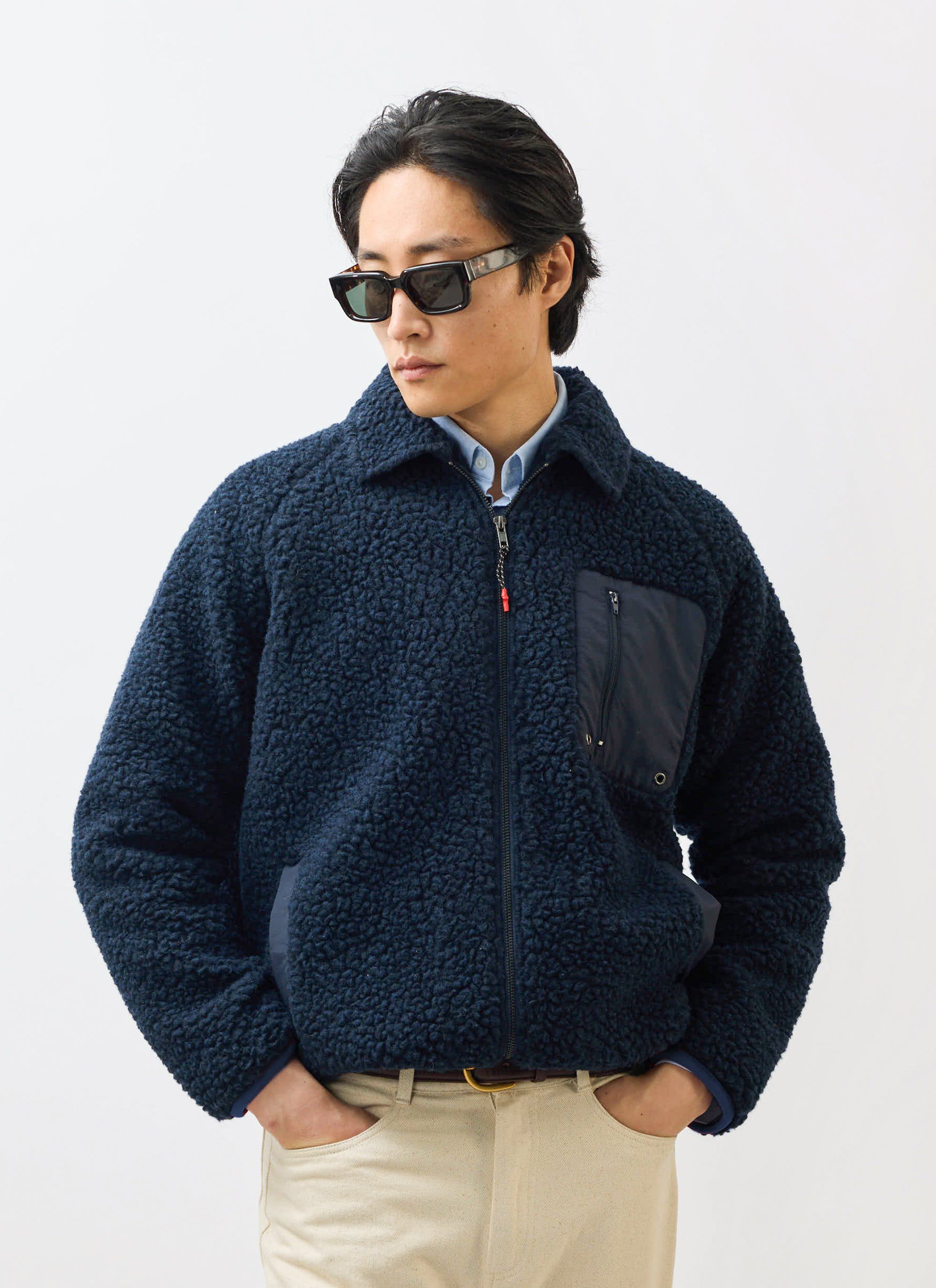 A model wears the Percival navy wool fleece jacket with sunglasses and cream trousers against a white background.