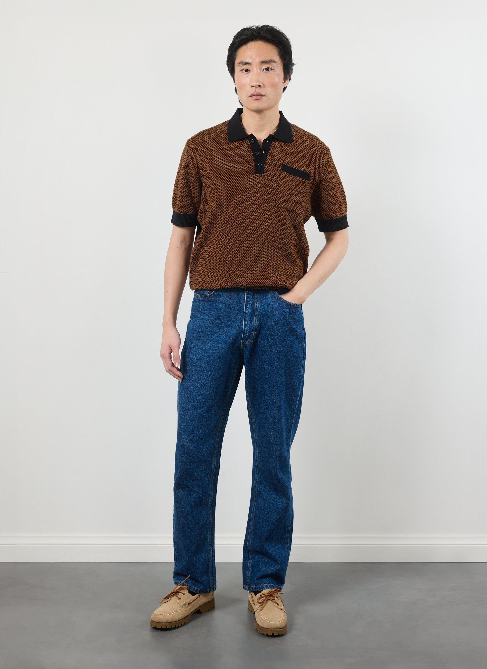 A model wears the Percival Casa Martini Knitted Polo in Espresso, styled with blue jeans and tan suede shoes.