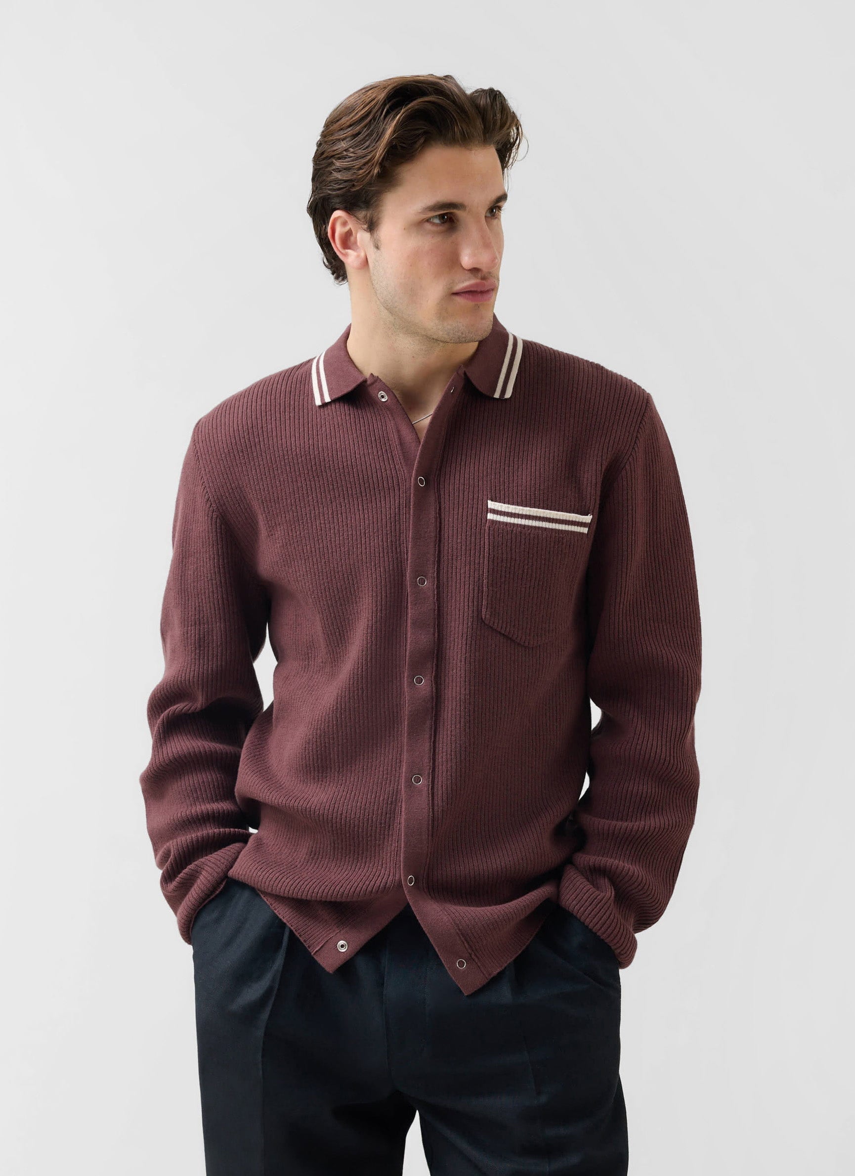 A man models the Percival Pablo long-sleeve knitted shirt in espresso brown with white tipping on the collar and pocket.