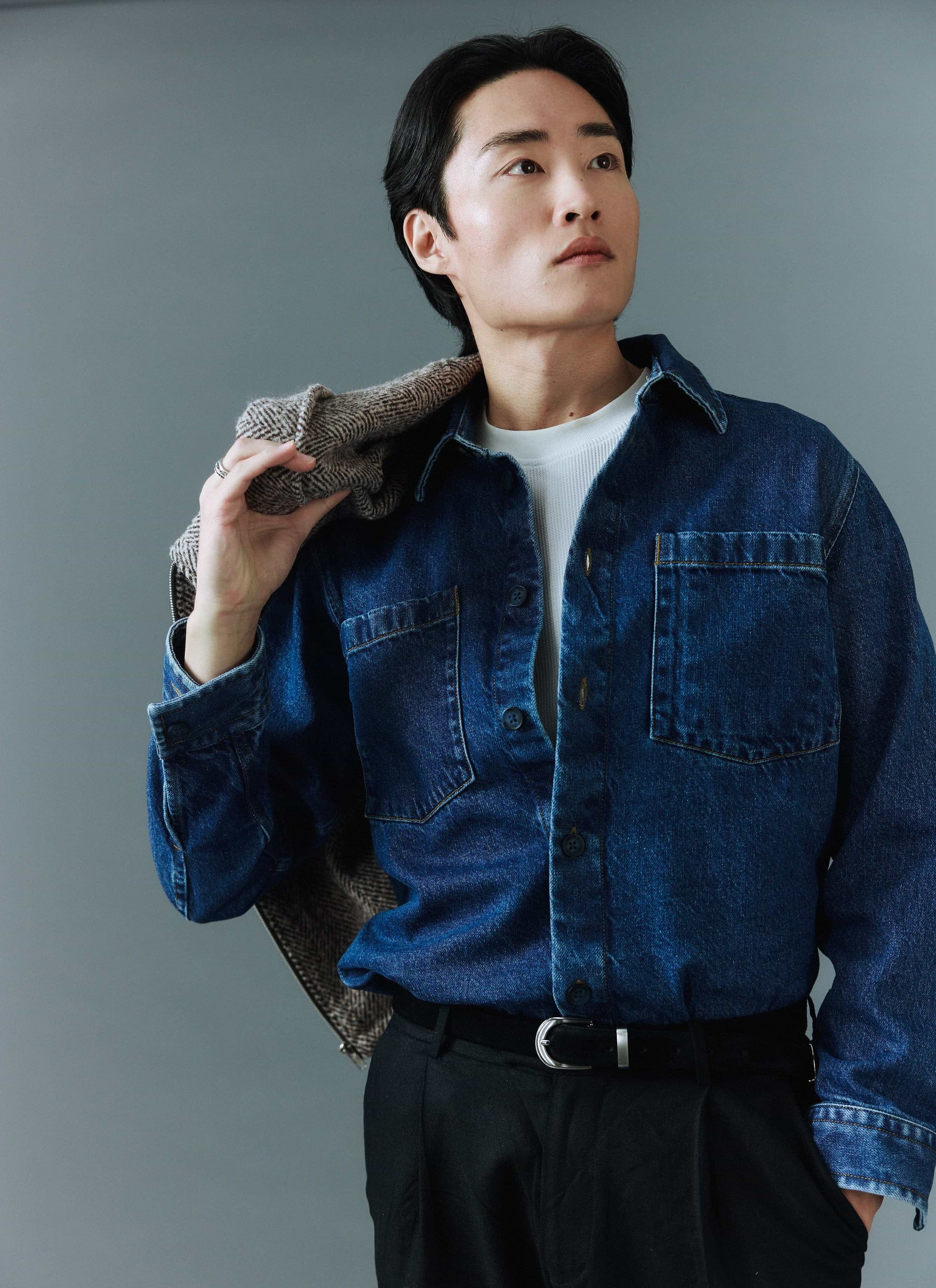 A model wears the Percival Denim Heavyweight Overshirt in mid-wash blue, holding a herringbone jacket over his shoulder.