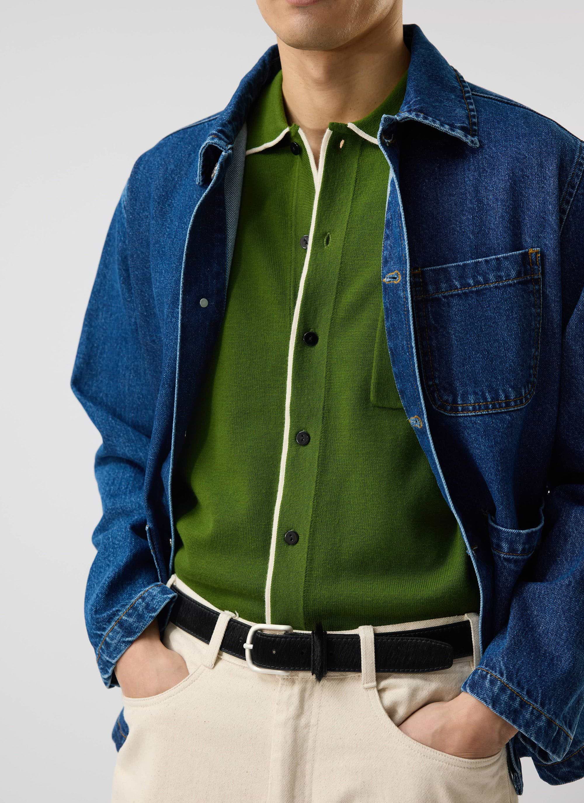 A model wears the Percival Contrast Trim Shirt in forest green, layered under a denim jacket with ecru trousers.