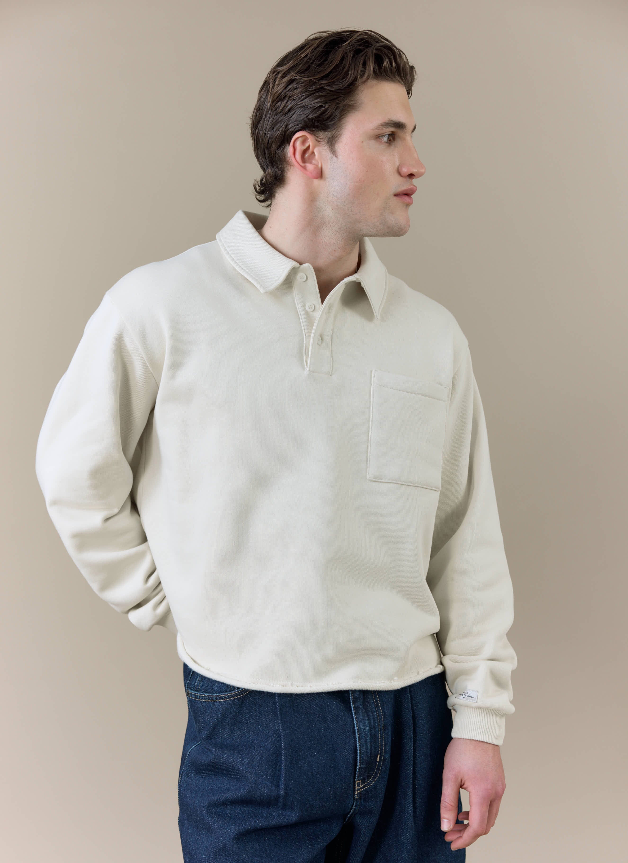 A side profile of a model wearing the cream Percival Dudley Boxy Sweatshirt, featuring a polo collar and chest pocket.