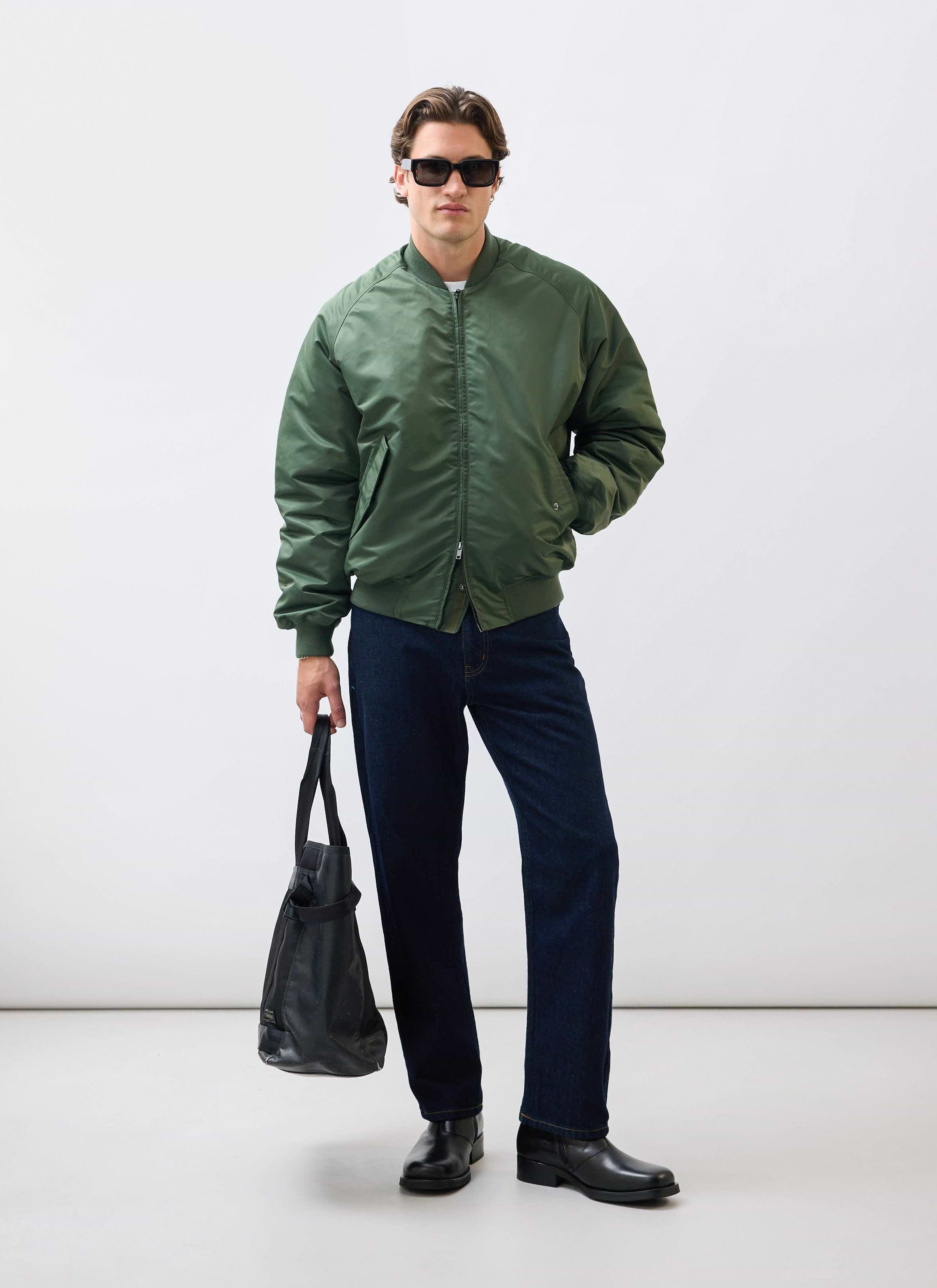 A model wears the Percival Nylon Bomber Jacket in Forest, styled with dark jeans, sunglasses and a black tote bag.