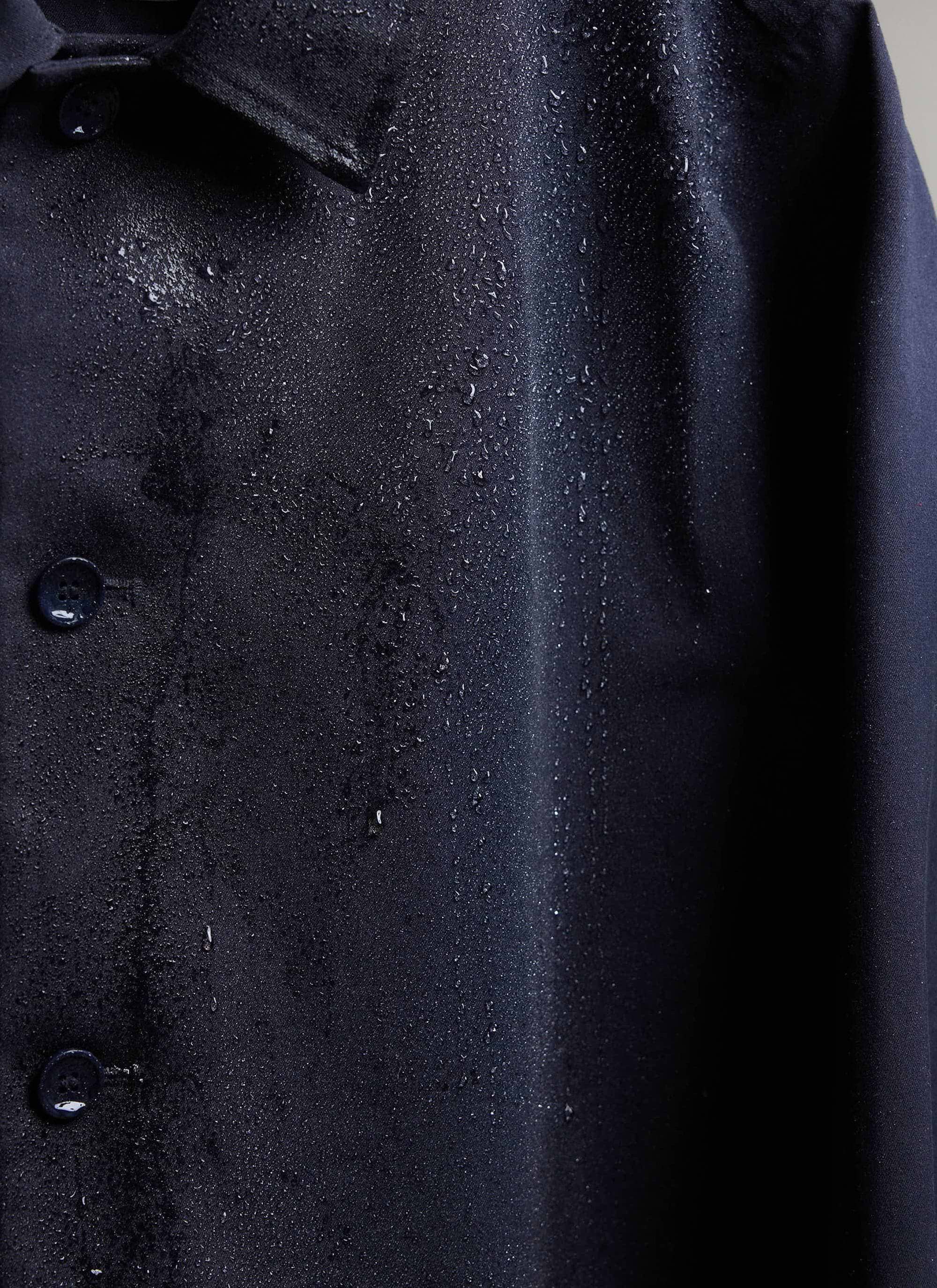 Close-up of the waterproof fabric on the navy Percival trench coat with water droplets.