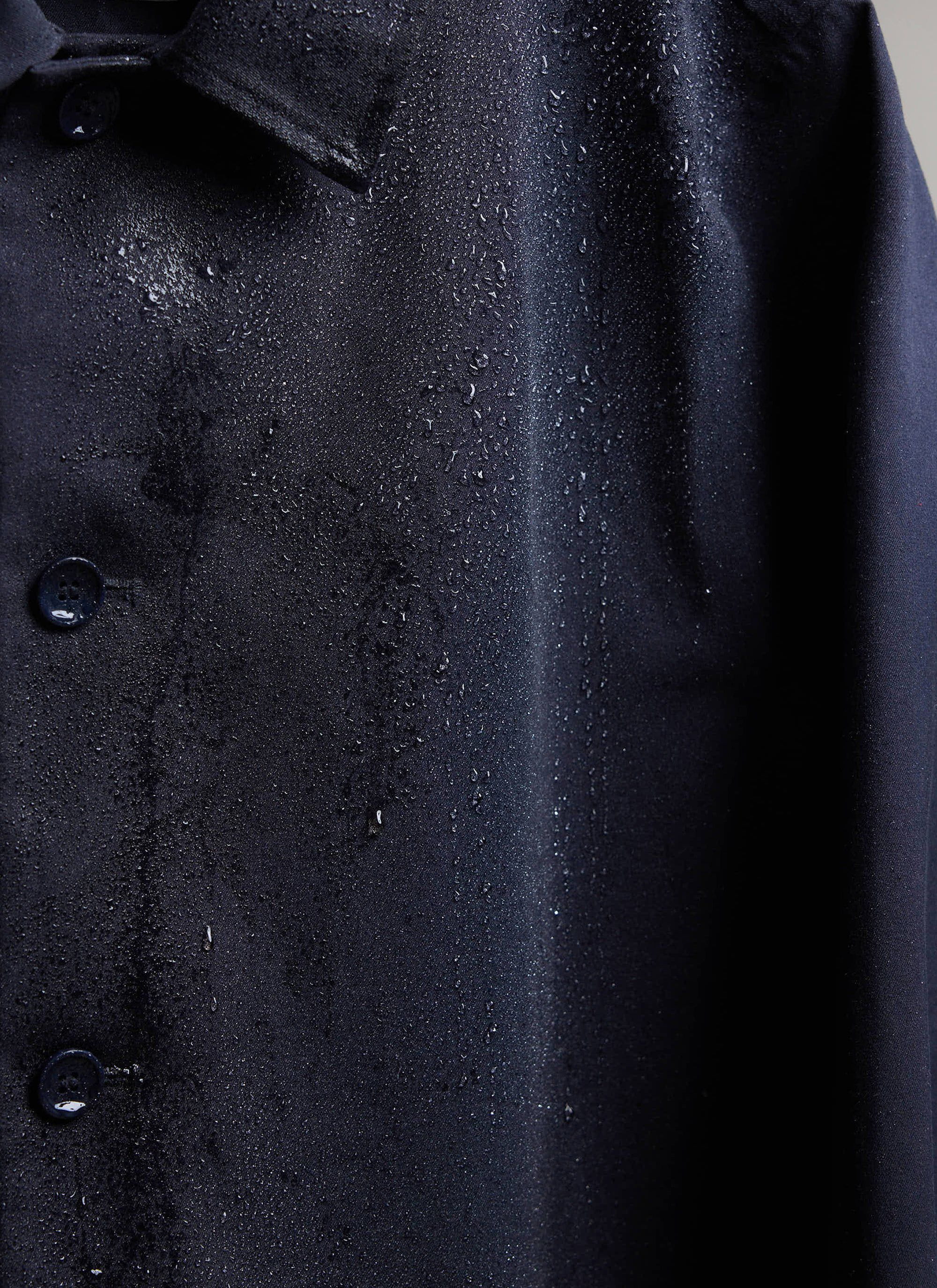 Close-up of the waterproof fabric on the navy Percival trench coat with water droplets.