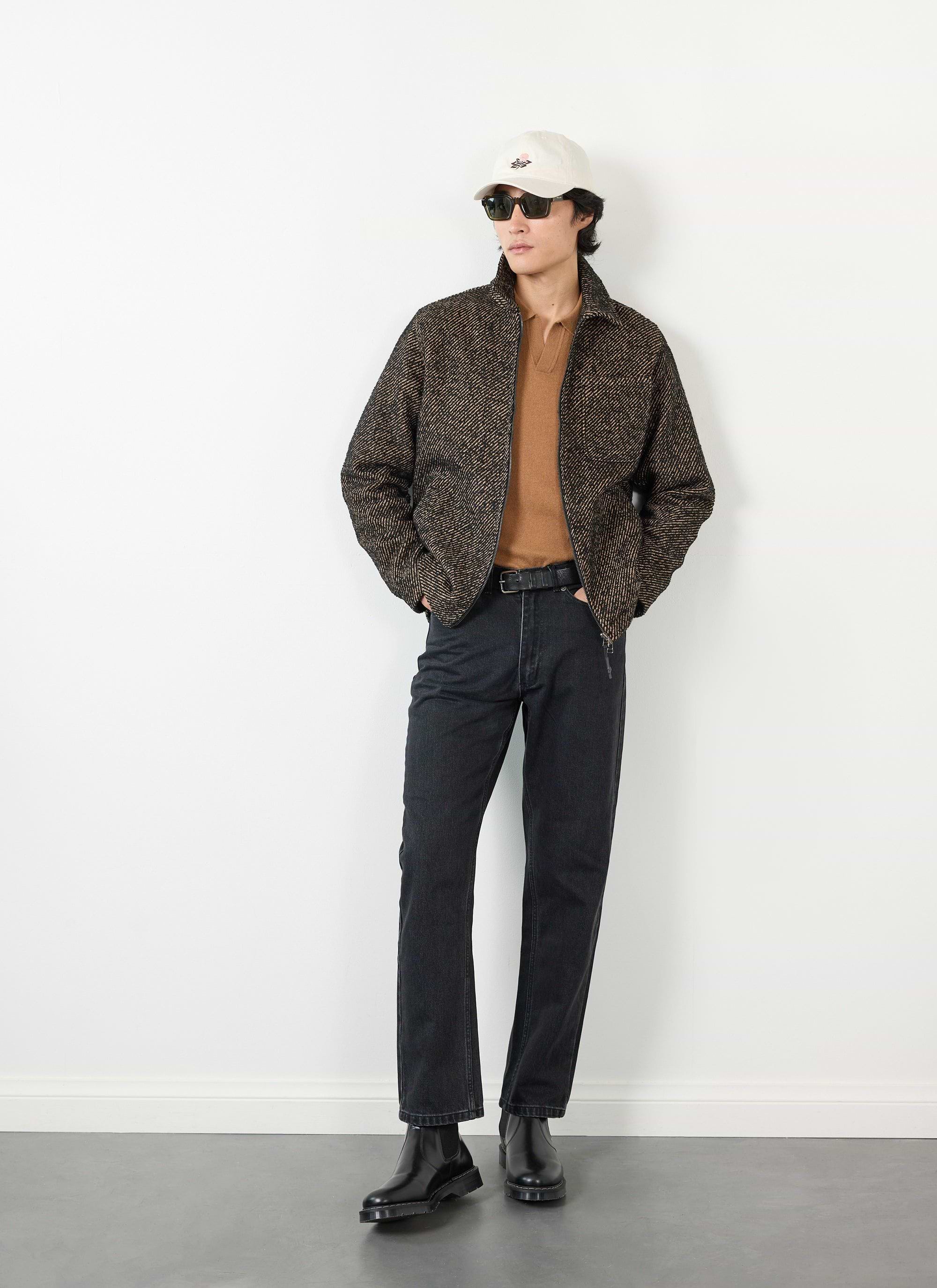 A model wears the Percival Zip Overshirt in Oak twill, styled with black jeans, a brown top, and a white cap.