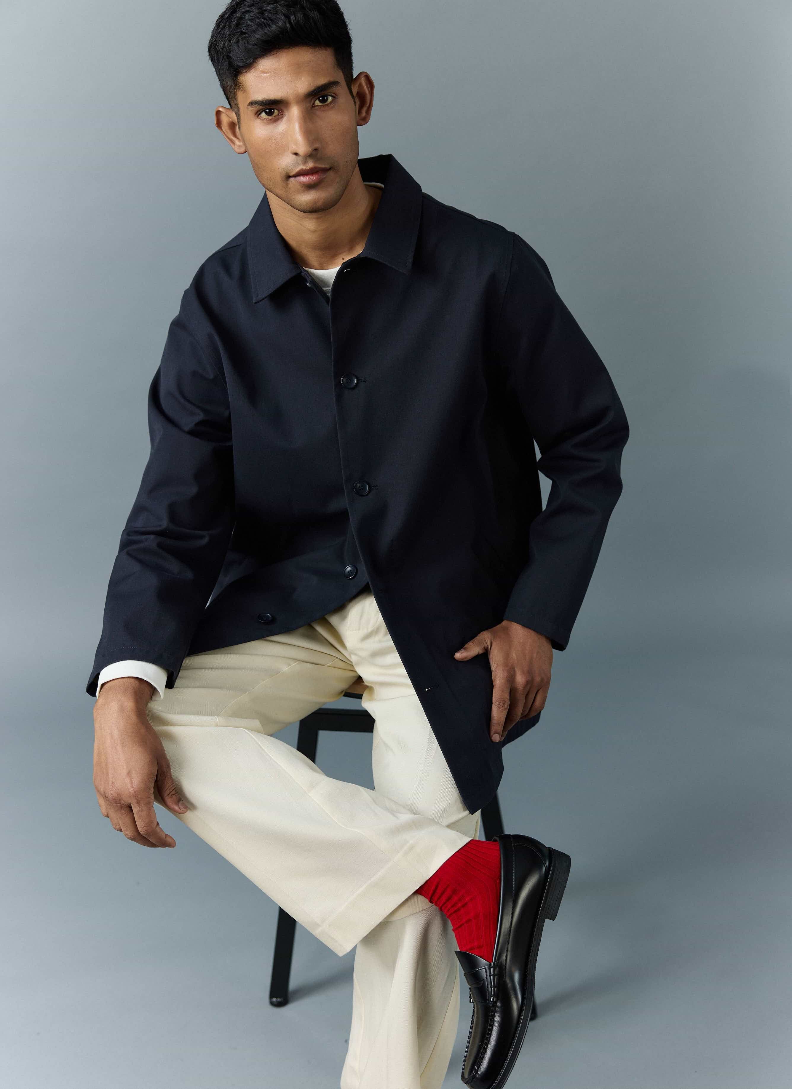 A model sits wearing the Percival Navy Sherlock Short Trench Coat, styled with cream trousers and red socks.