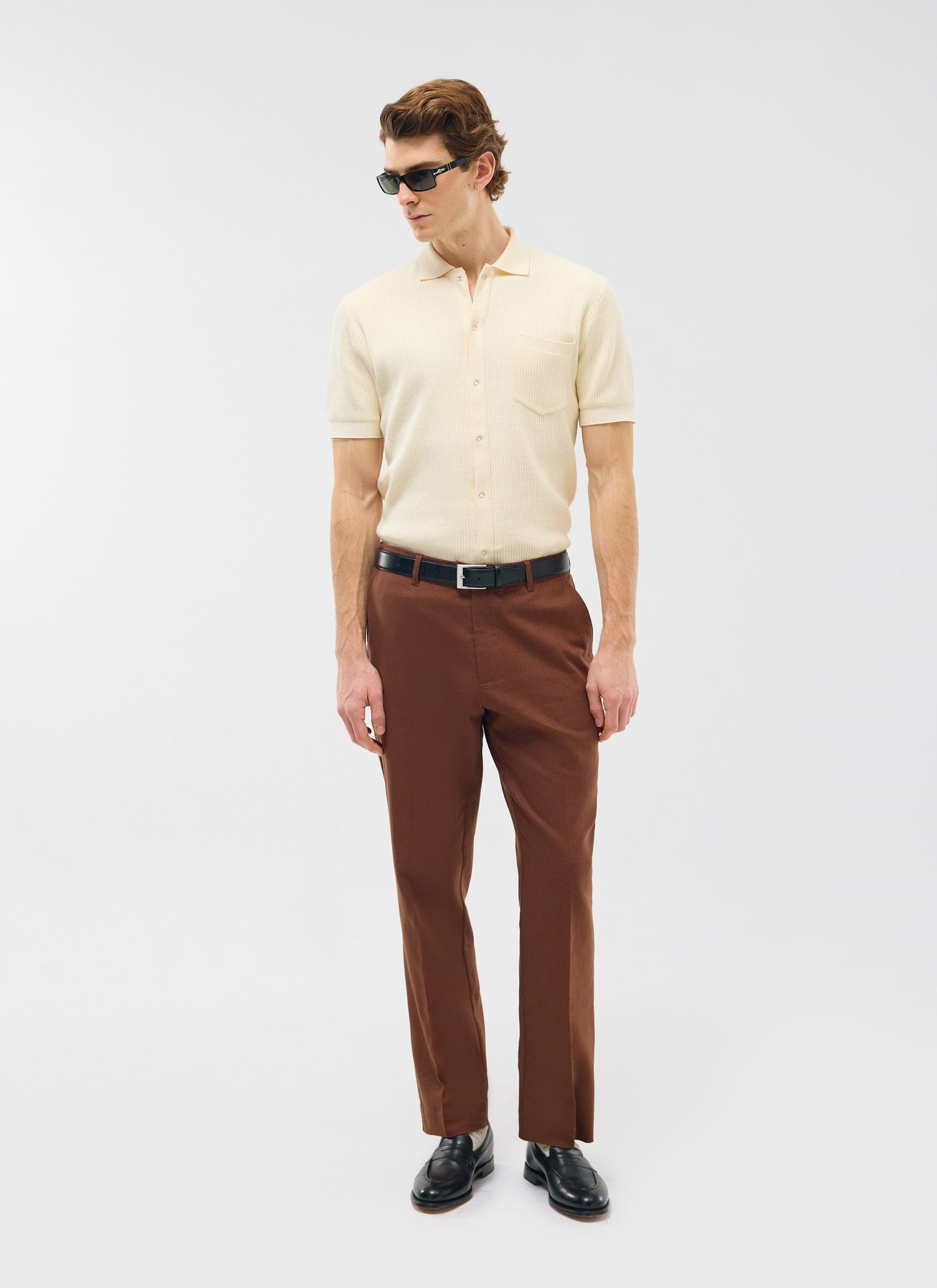 Percival Tailored Linen Trousers in brown, styled on a model with a cream knitted polo shirt, black loafers, and sunglasses.