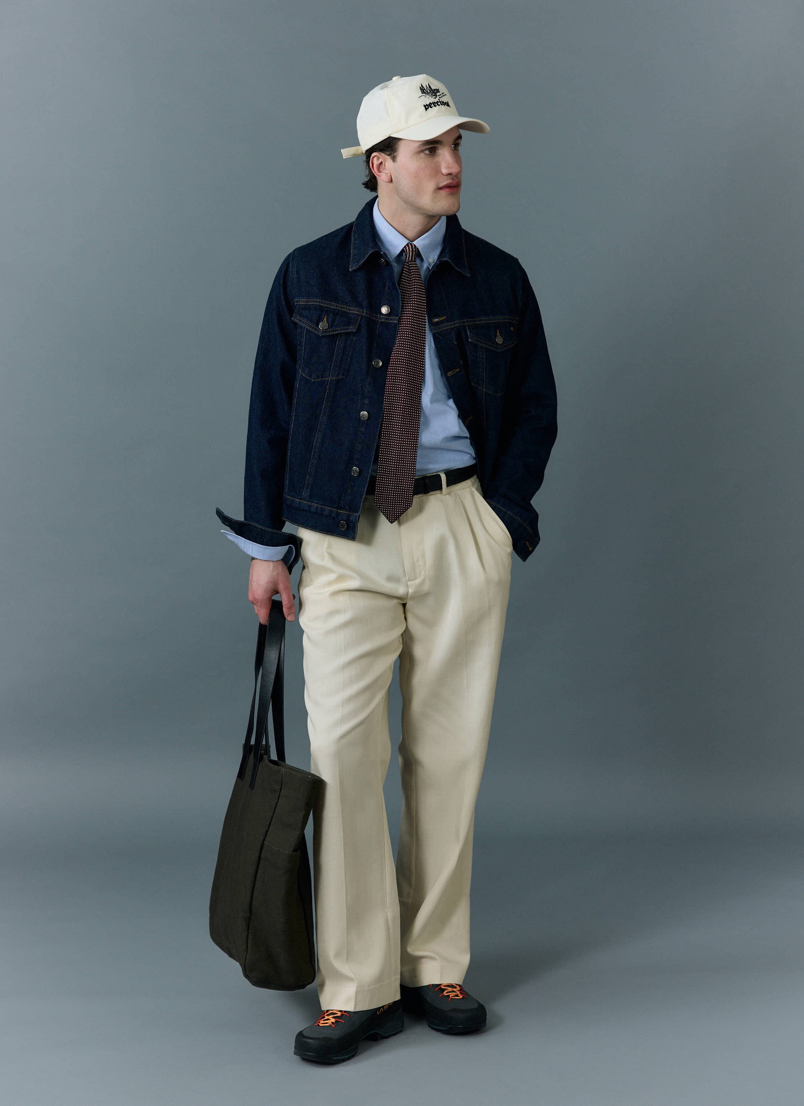 A man models the Percival Western Trucker Jacket in Dark Indigo, styled over a shirt and tie with cream trousers.
