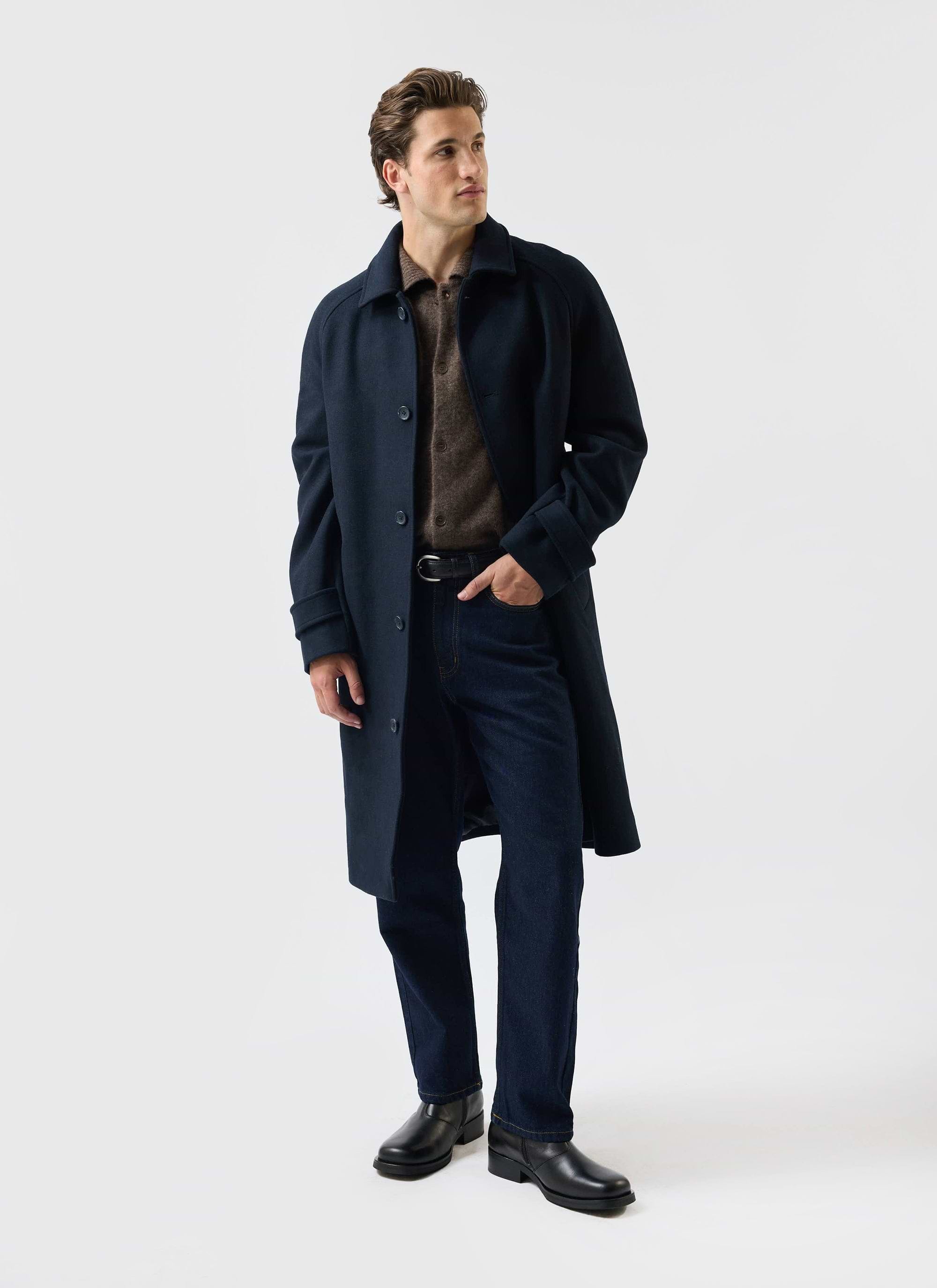 A model styles the navy wool car coat from Percival, worn over a brown knitted polo shirt and dark wash jeans.
