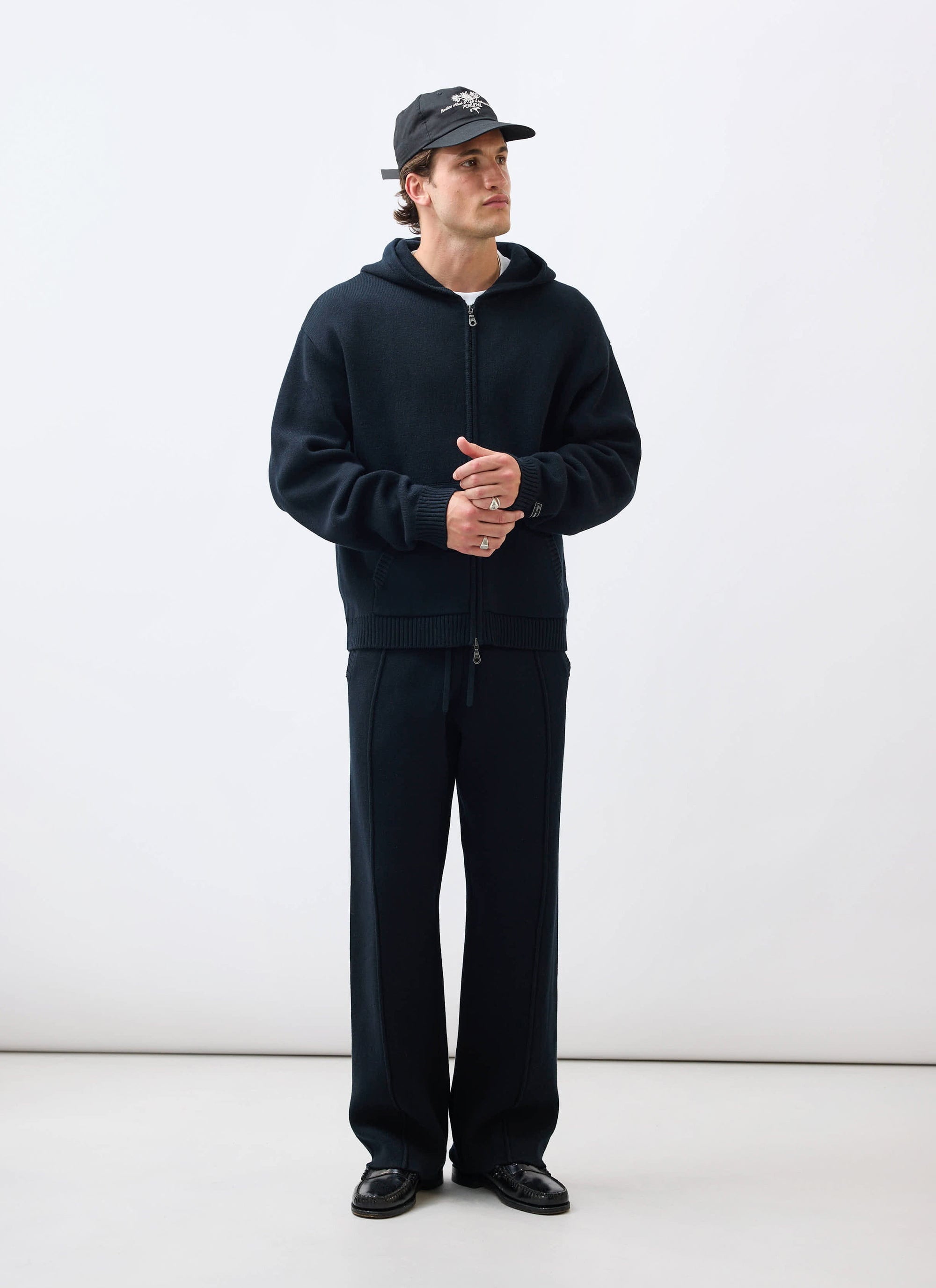 A model wears the black Chronicle Knitted Hoodie with matching trousers from Percival against a white background.