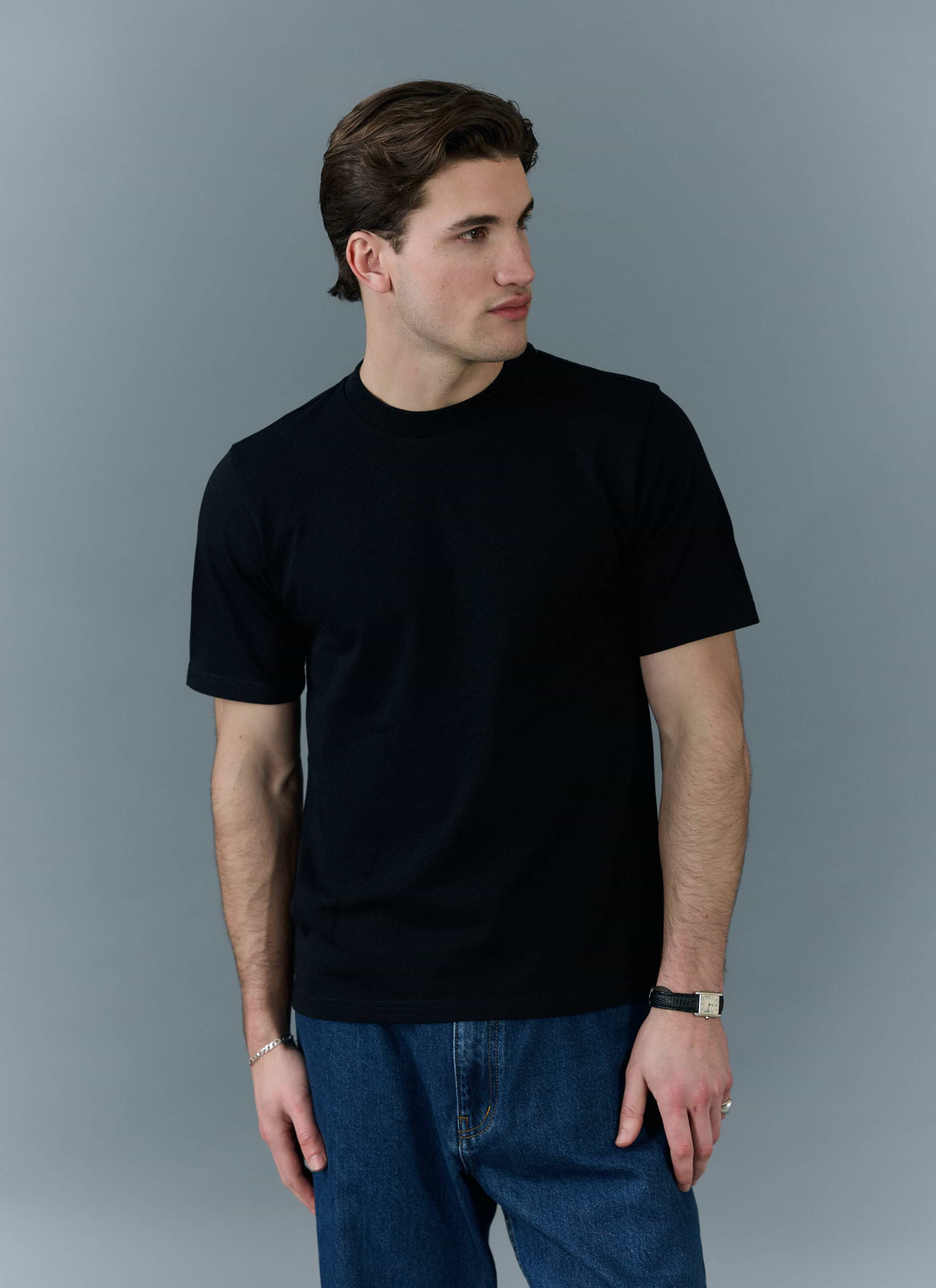 A man models the Percival black Cropped Regular Fit T-Shirt, styled with blue jeans against a simple grey background.