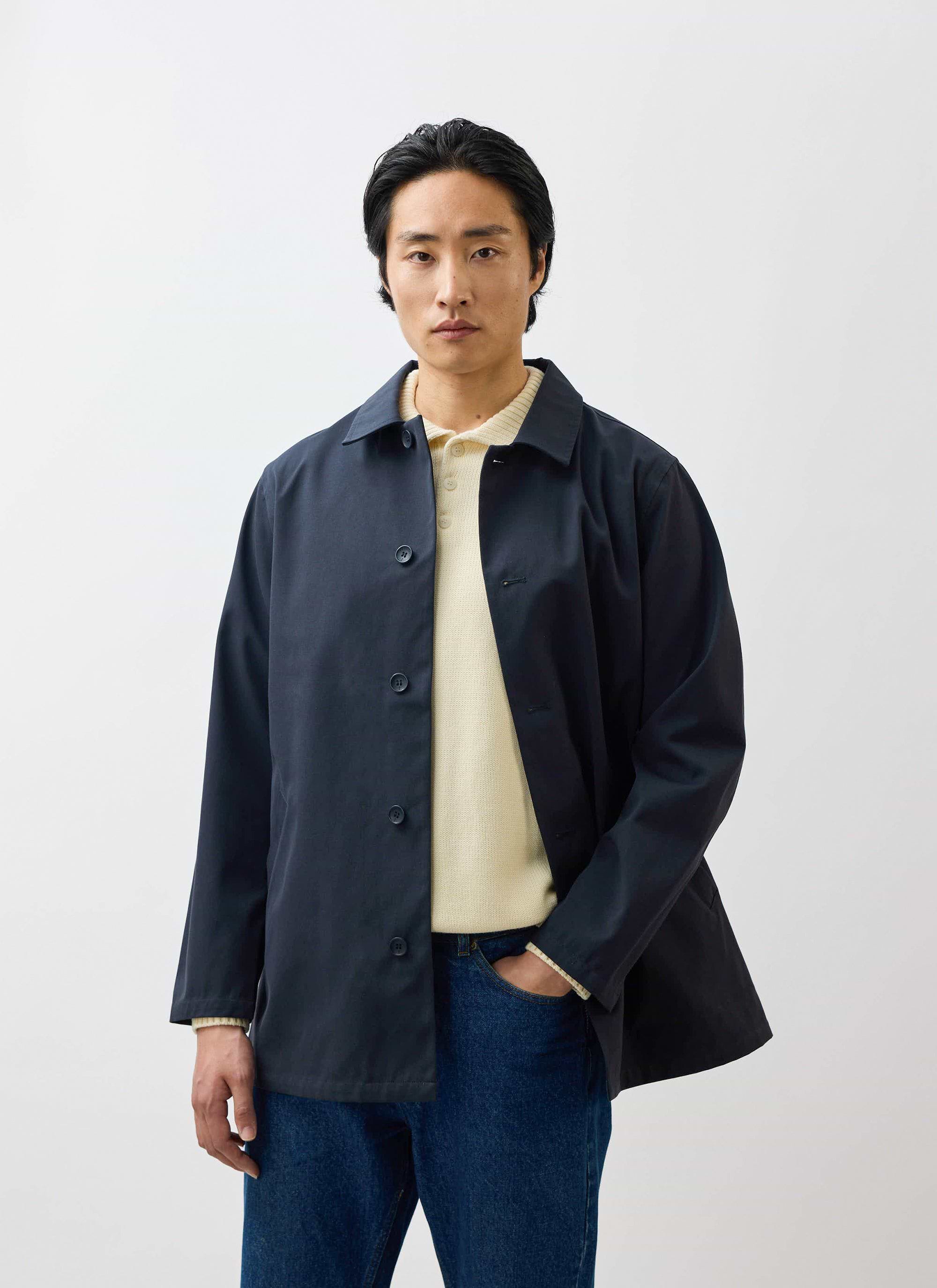 A model wearing the waterproof Percival Sherlock Short Trench Coat in midnight, styled with a cream knit and blue jeans.