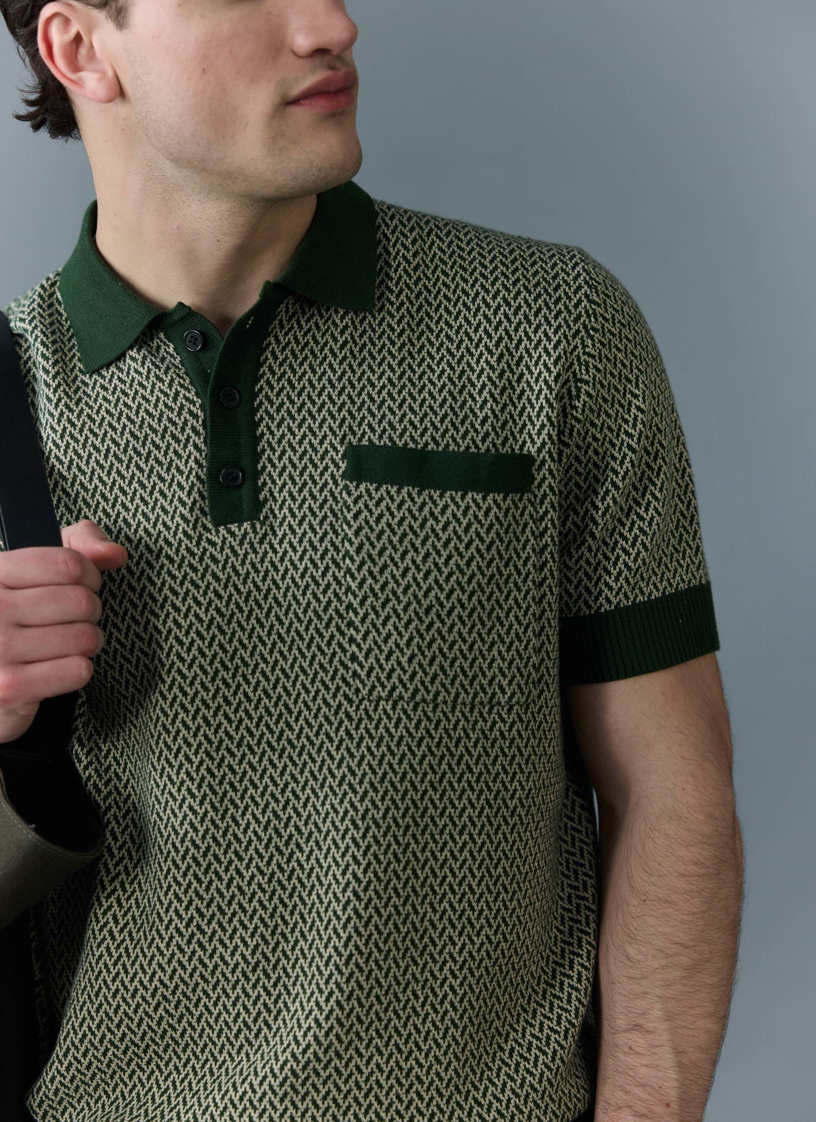 A man models the Percival Casa Martini Knitted Polo in forest green, which has a cream geometric pattern and a chest pocket.