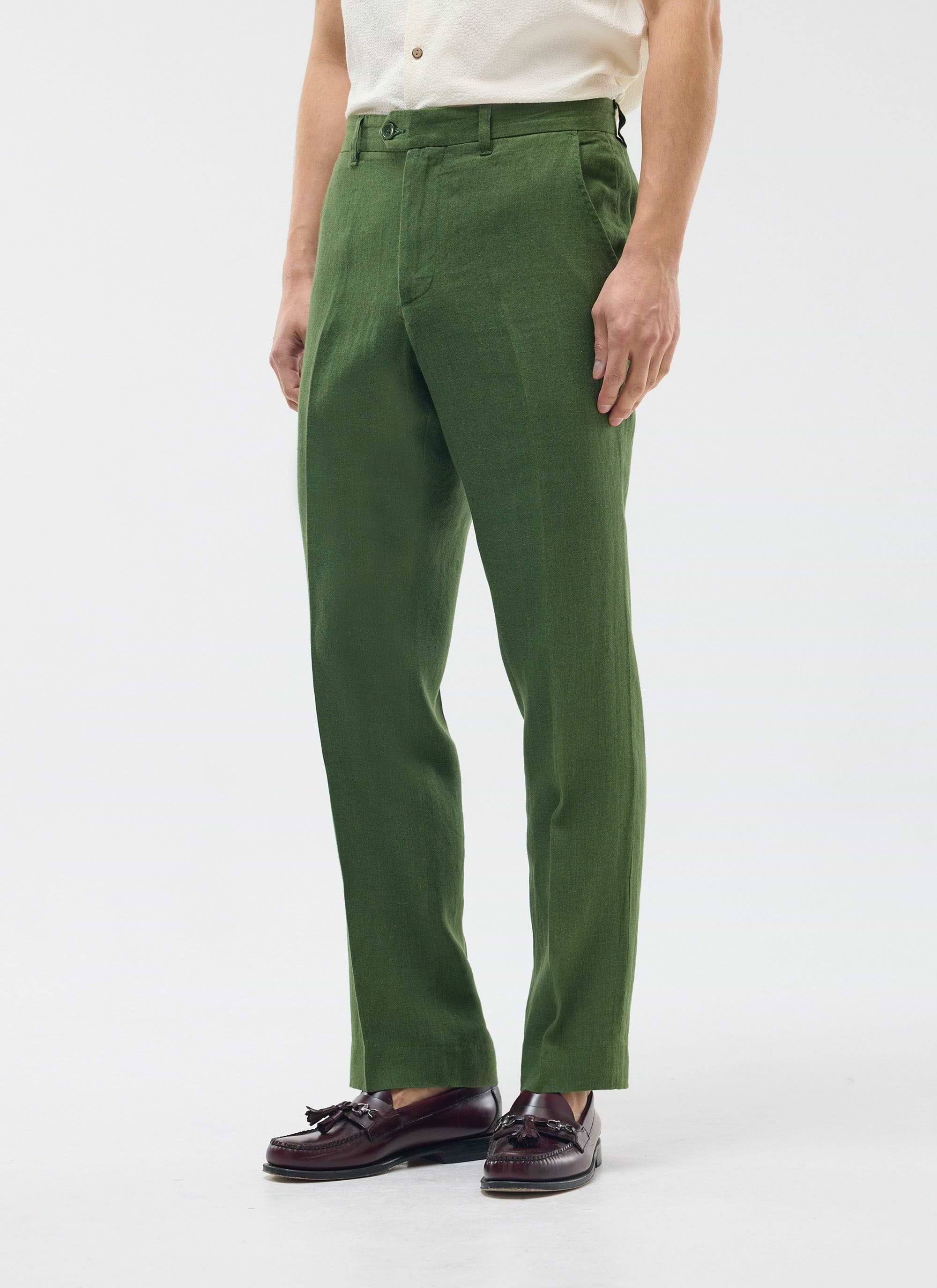 A model wears Percival's forest green tailored linen trousers with a cream shirt and dark brown tassel loafers.