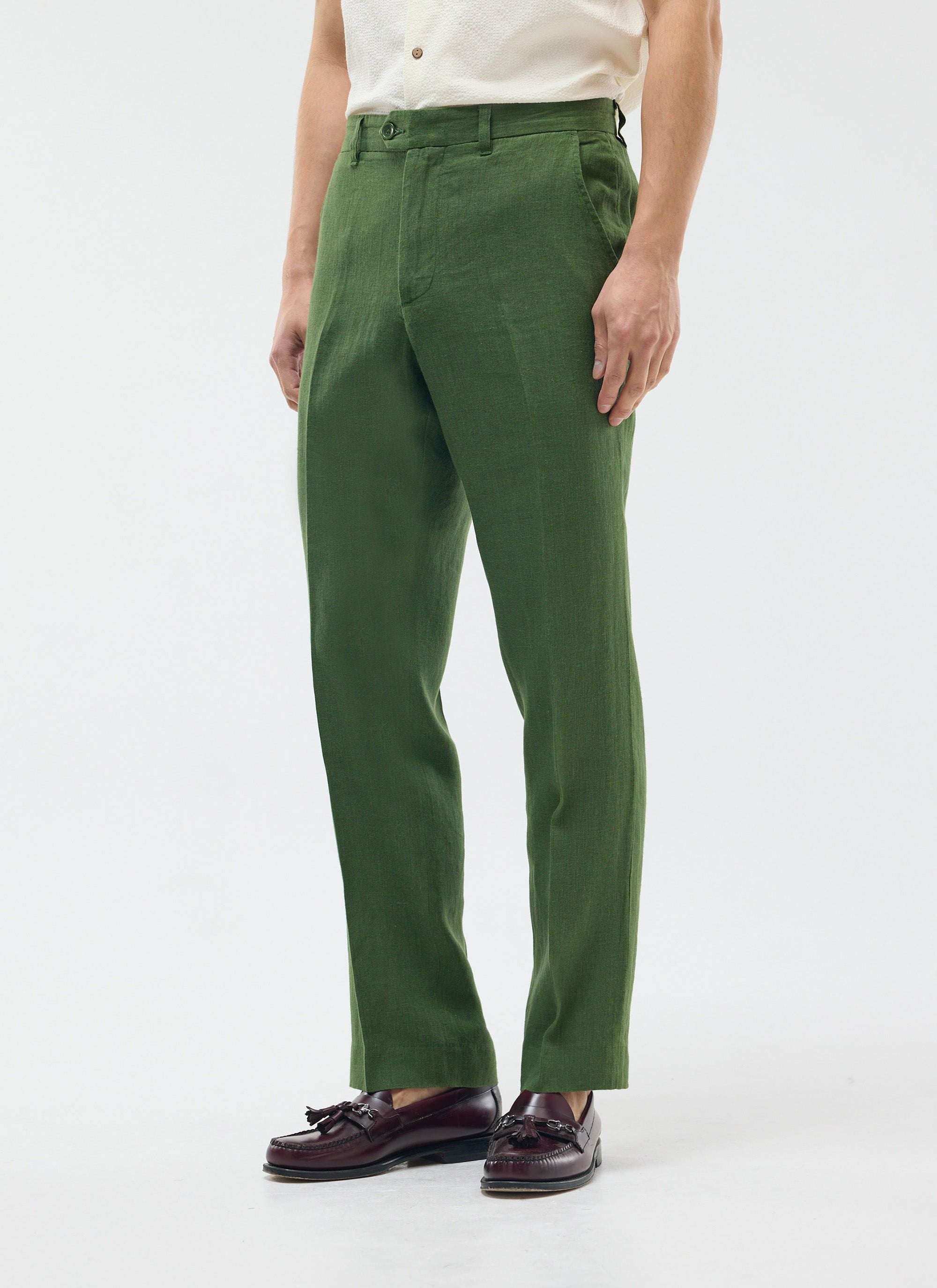 A model wears Percival's forest green tailored linen trousers with a cream shirt and dark brown tassel loafers.