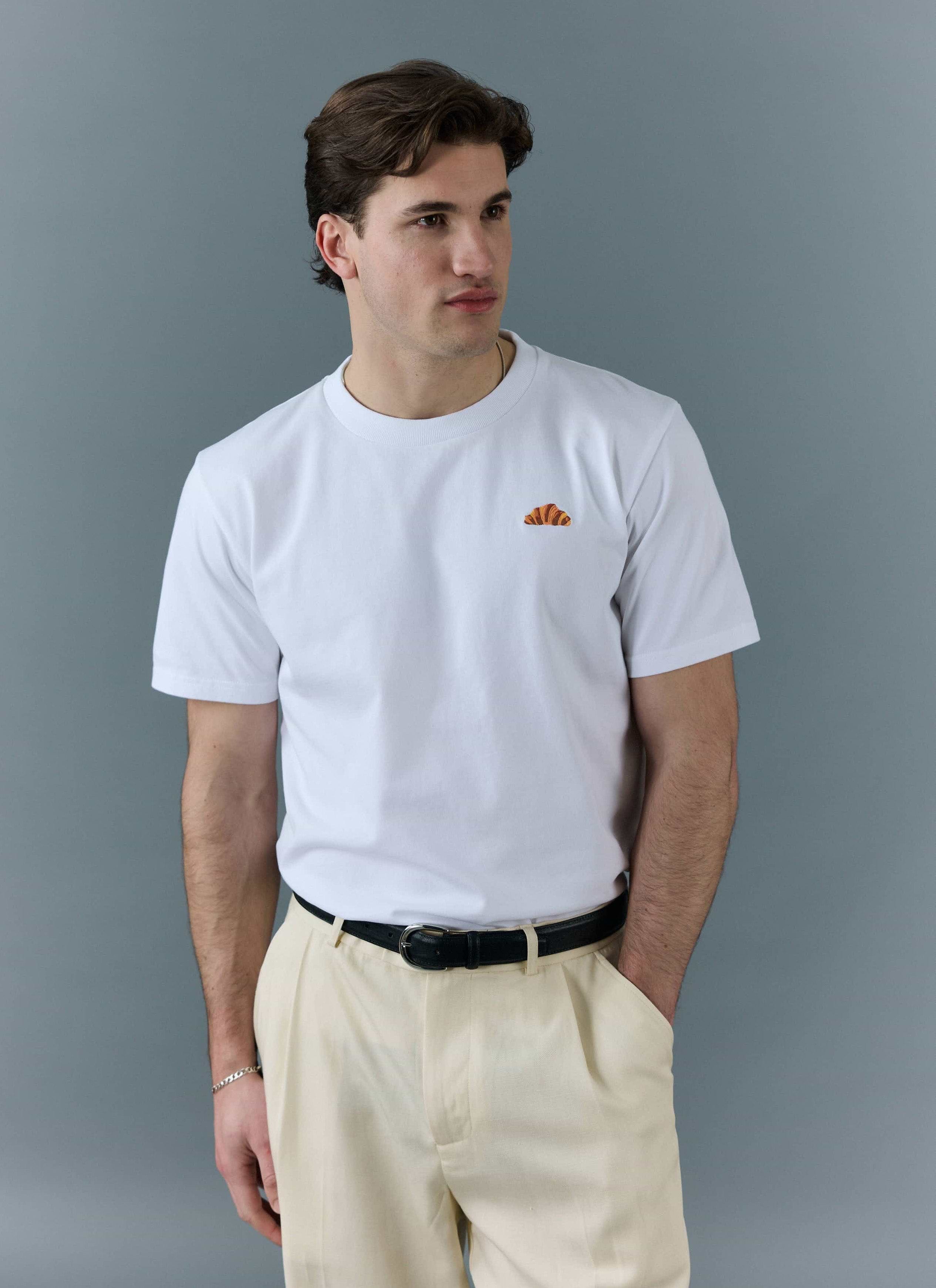 A model wears the Percival white t-shirt with an embroidered croissant on the chest, styled with cream trousers.