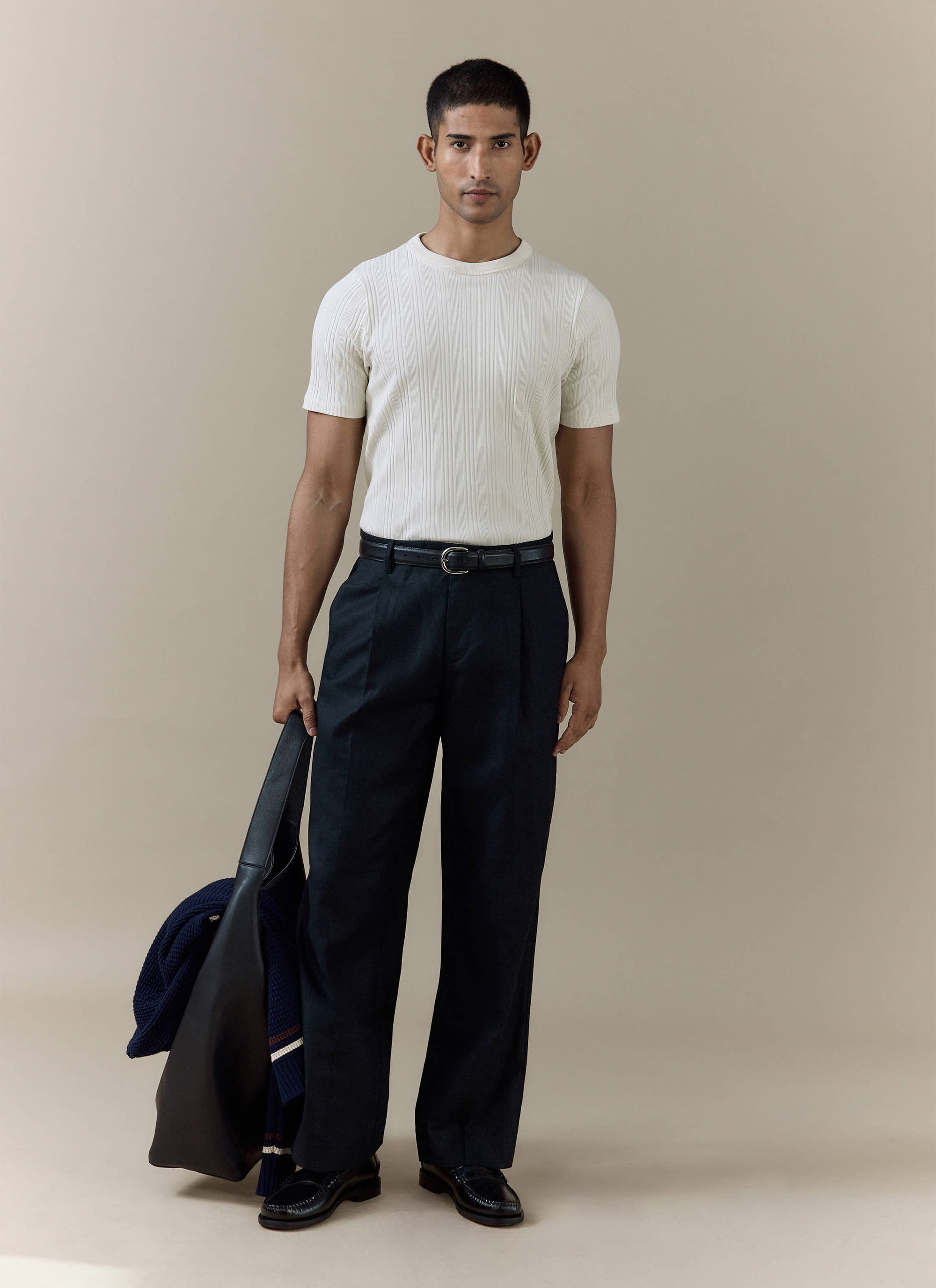 The Percival Leon Ribbed T Shirt in cream cotton worn by a model with dark trousers and a black leather bag.