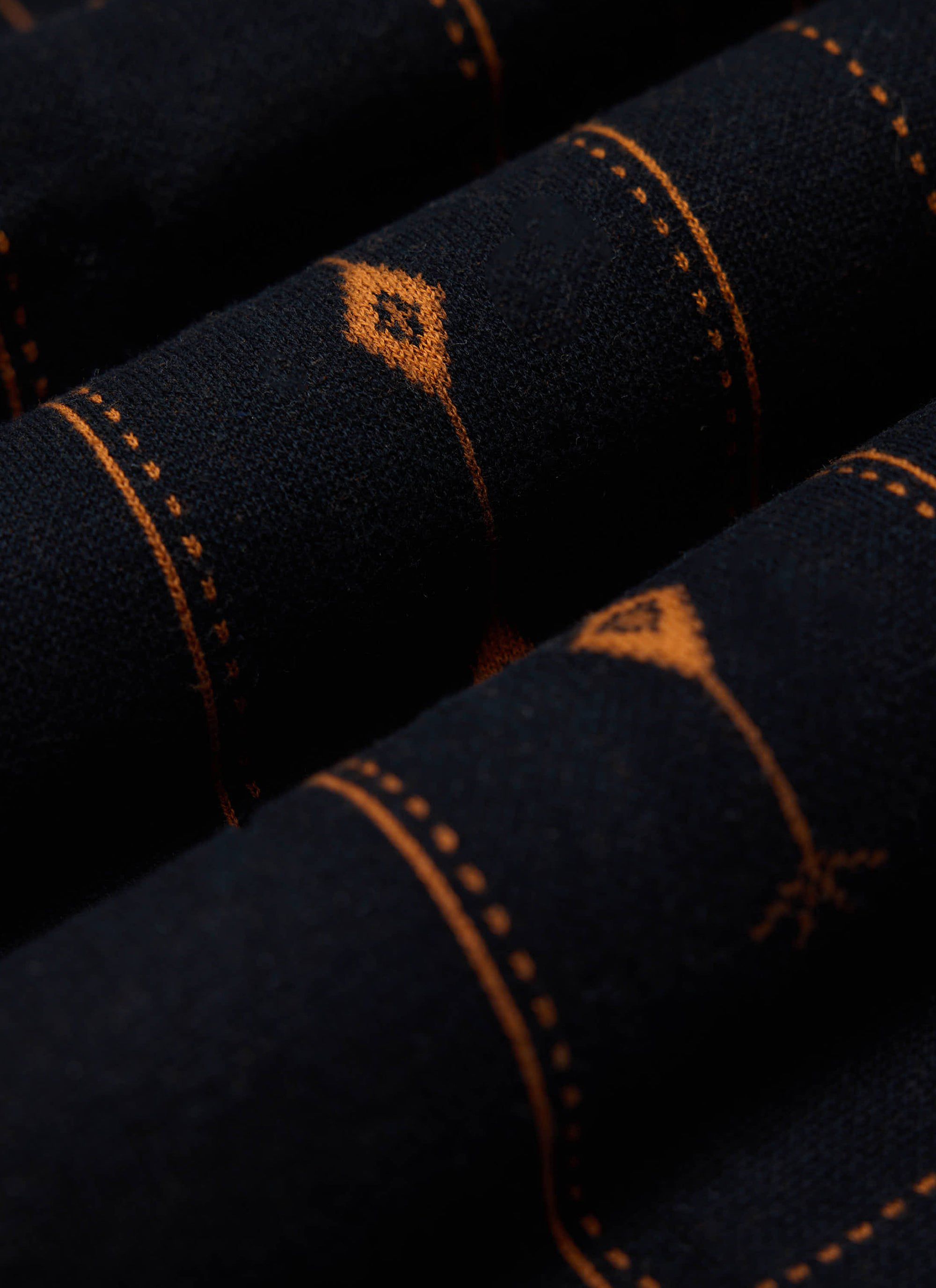 A close-up shot of the folded dark navy Percival Folio Knitted Shirt, detailing the tobacco book spine jacquard knit.