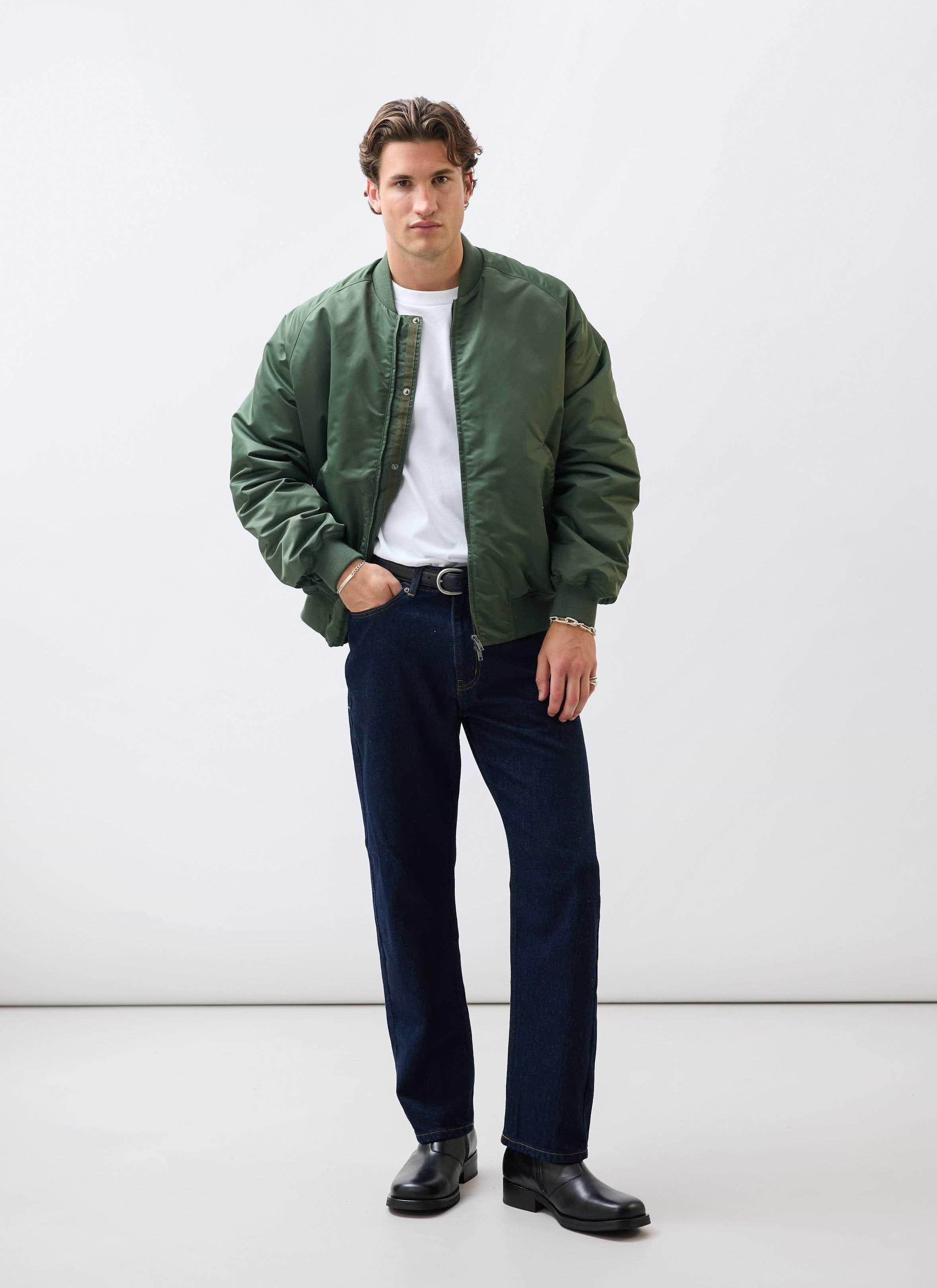 A male model wears the Percival forest green nylon bomber jacket, styled with a white t-shirt and dark jeans.